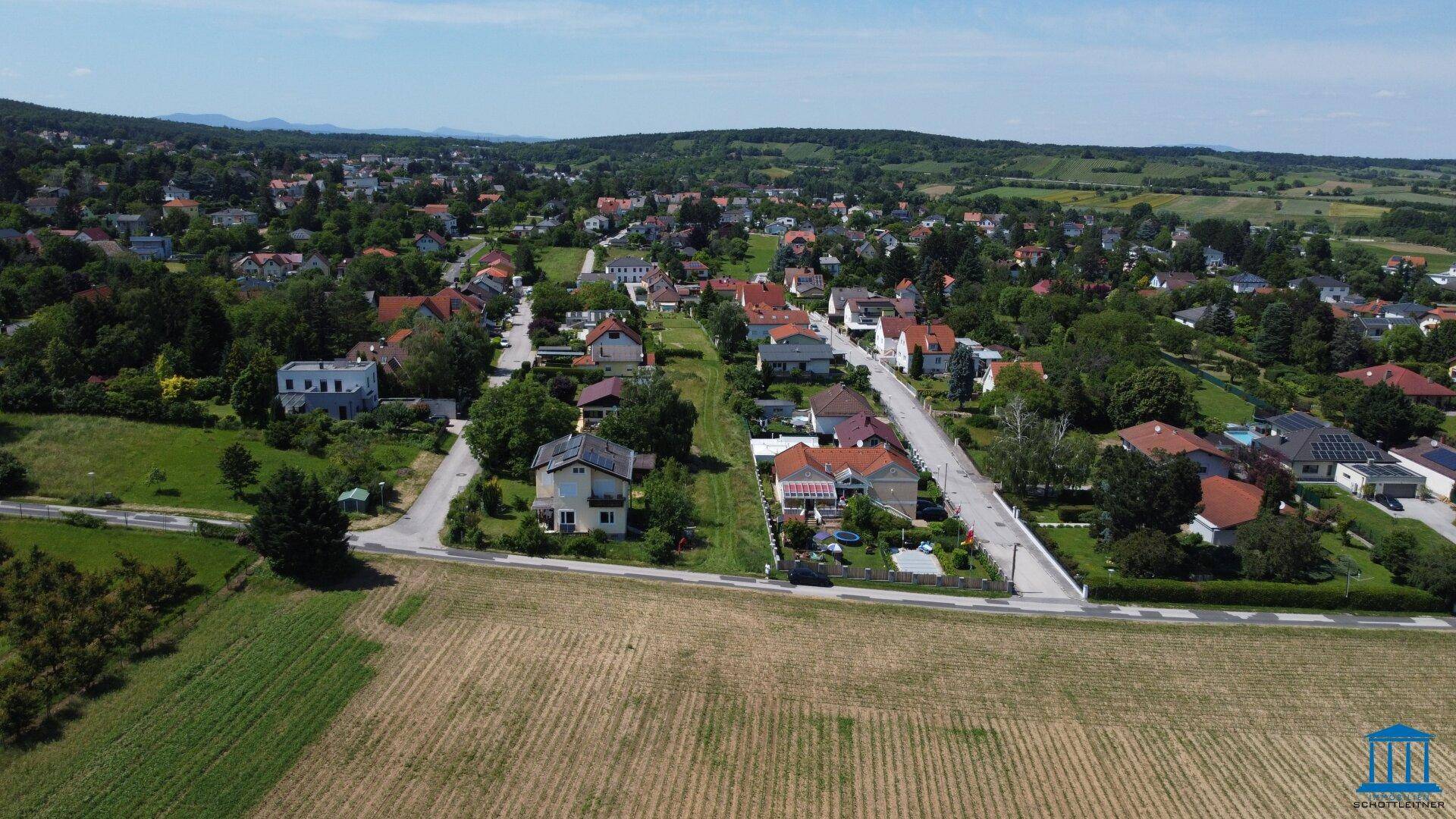 Panoramische Luftansicht eines Dorfes mit vielen Häusern, umgeben von Feldern und grünen Hügeln.