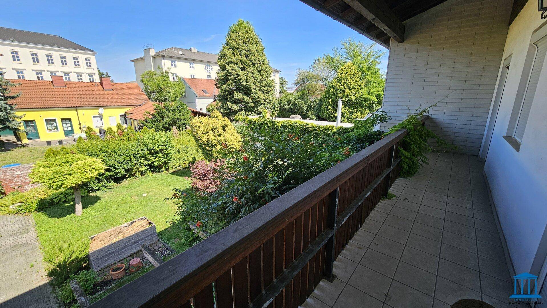 Balkon mit Fliesenboden und Holzgeländer, bietet einen schönen Blick auf den grünen Garten.