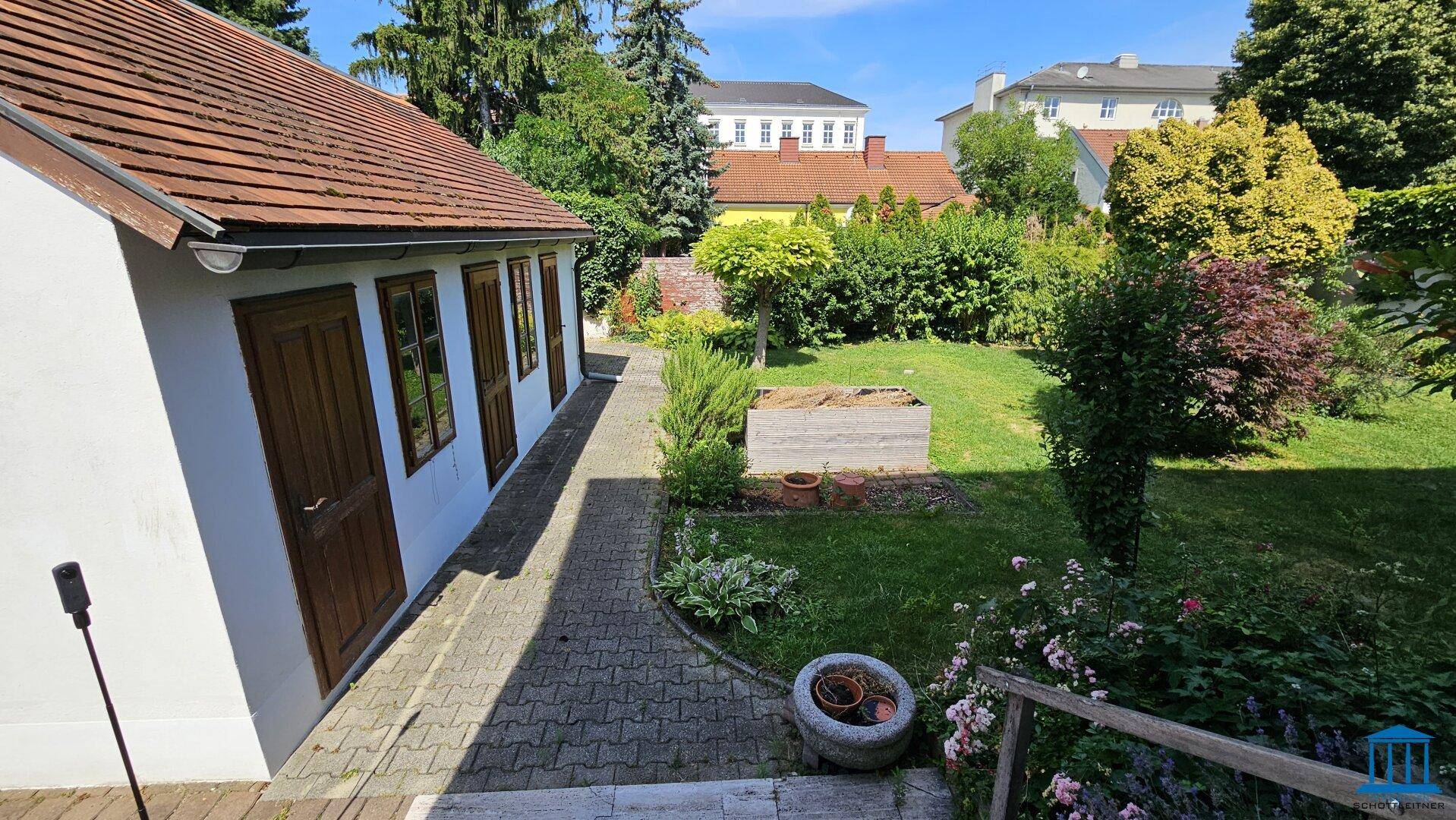 Gartenansicht mit einem kleinen Nebengebäude und einem gepflasterten Zugangsweg.