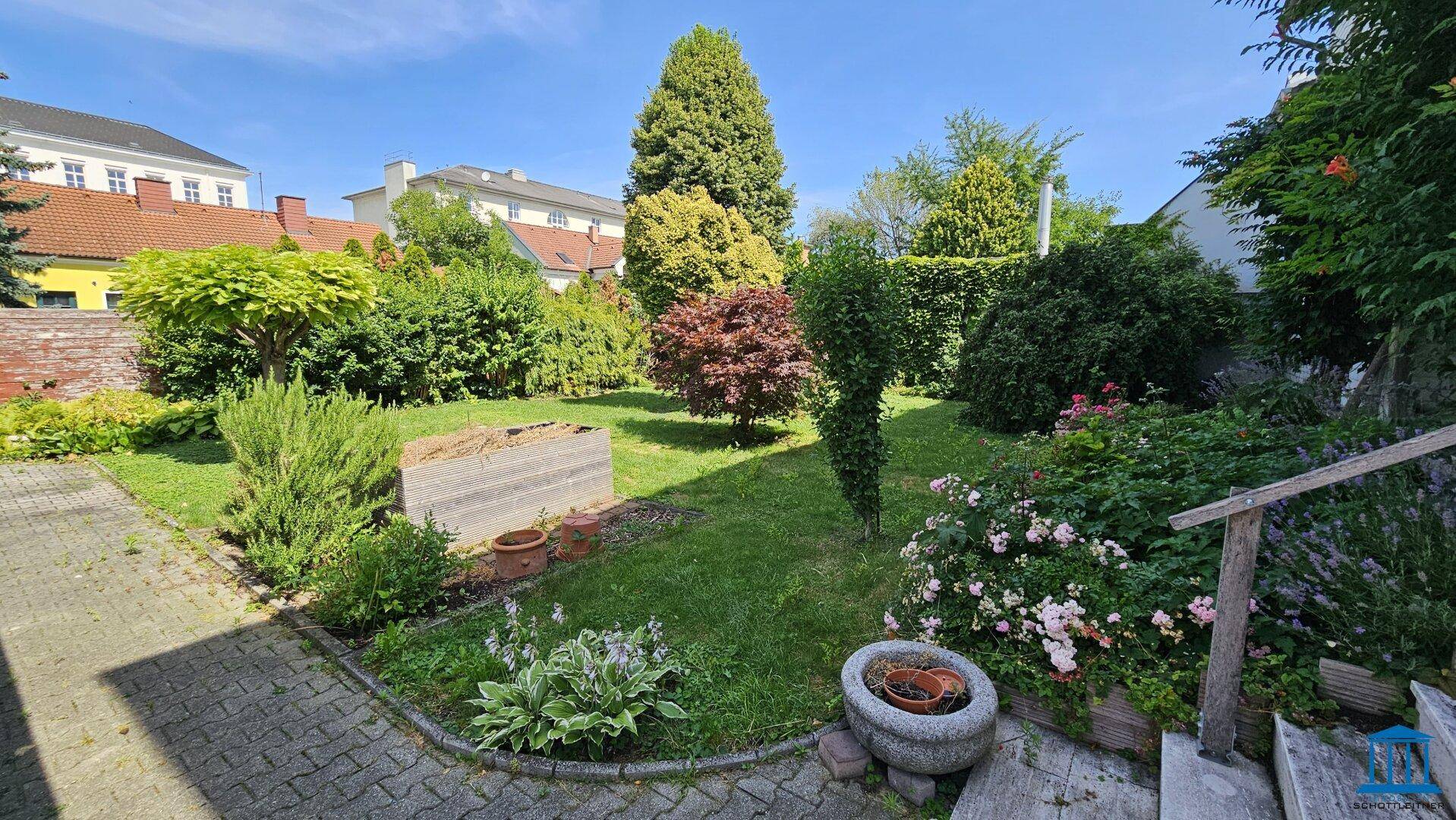 Idyllischer Gartenbereich mit gepflastertem Weg, Blumenbeeten und üppiger Vegetation.