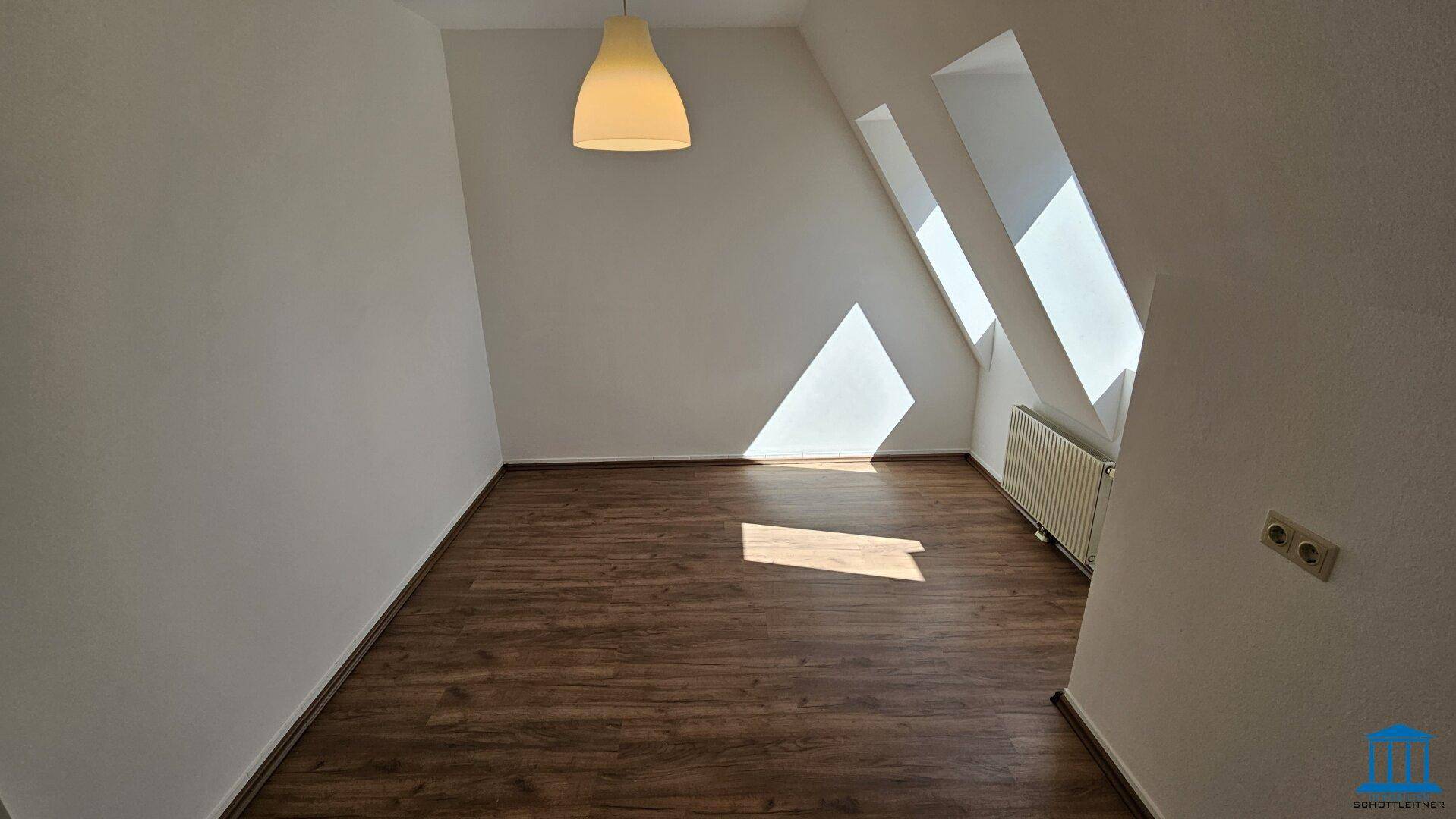 Dachgeschosszimmer mit schrägen Fenstern, Laminatboden und viel natürlichem Licht.