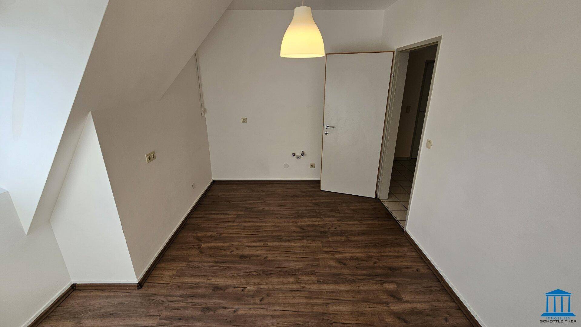 Helles Zimmer im Dachgeschoss mit Laminatboden und Zugang zu weiteren Räumen.