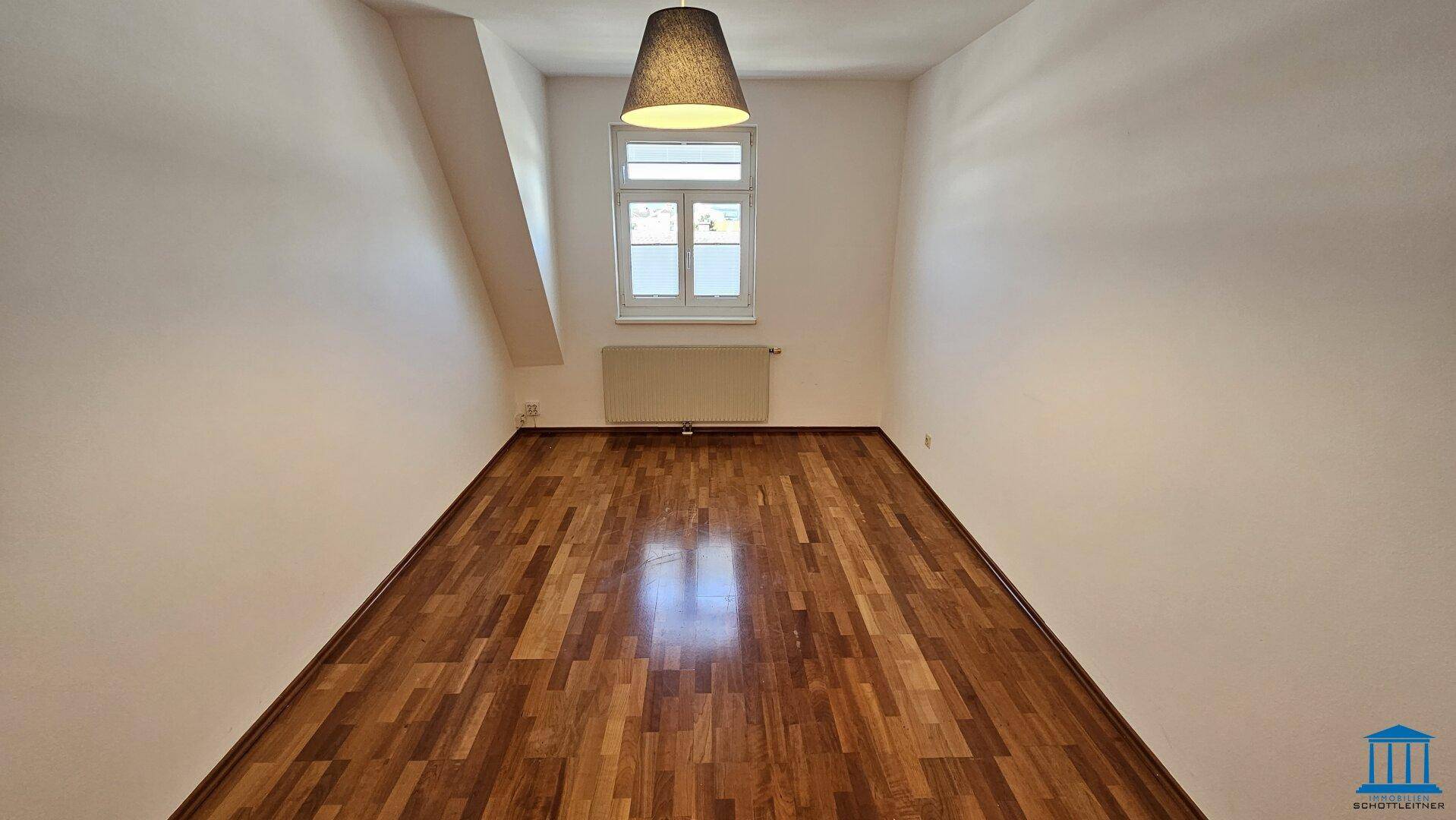 Gemütliches Zimmer im Dachgeschoss mit Parkettboden, einem Fenster und schrägen Wänden.