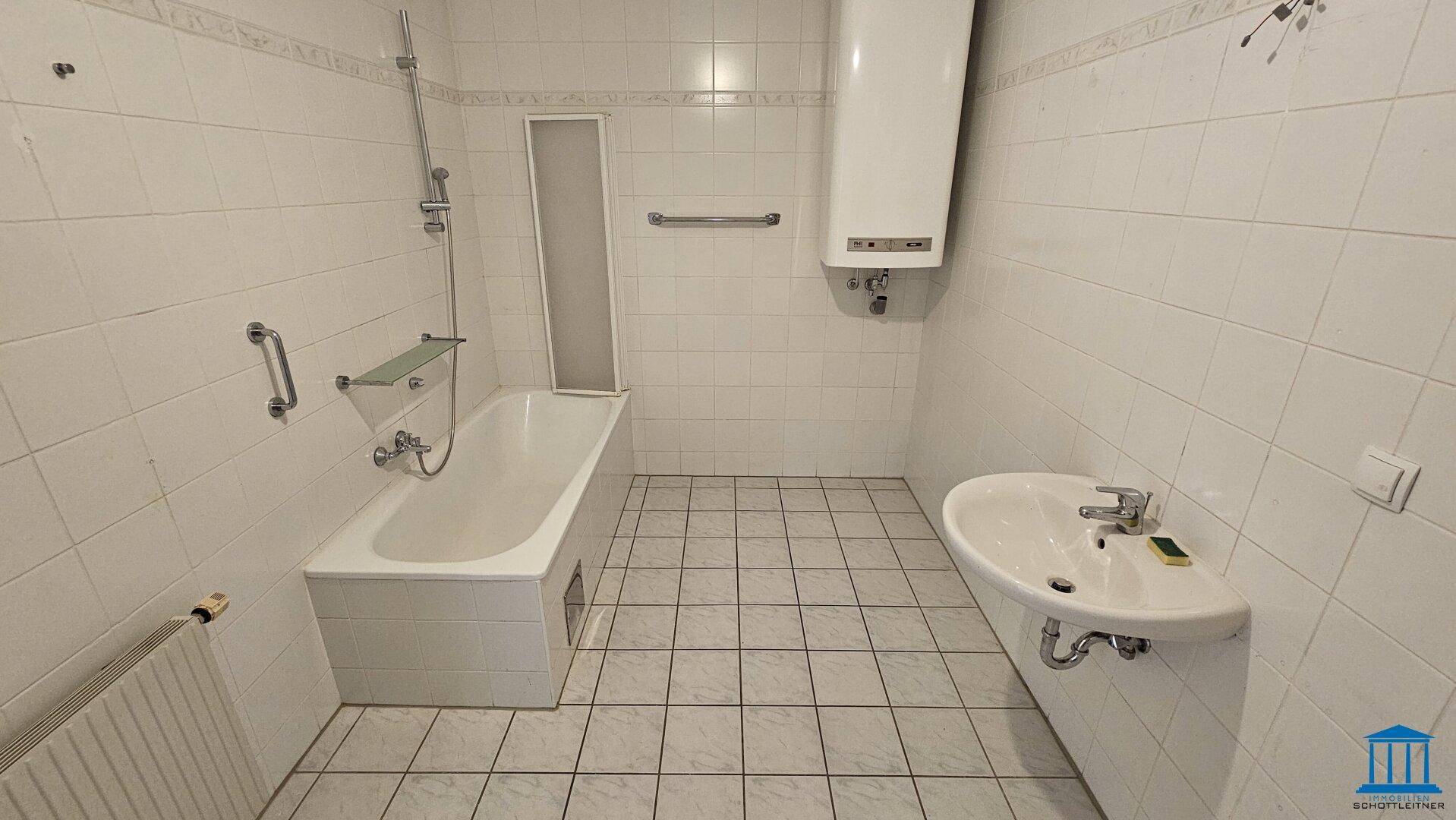 Gefliestes Badezimmer mit Badewanne, Duschfunktion, Waschbecken und Warmwasserboiler.