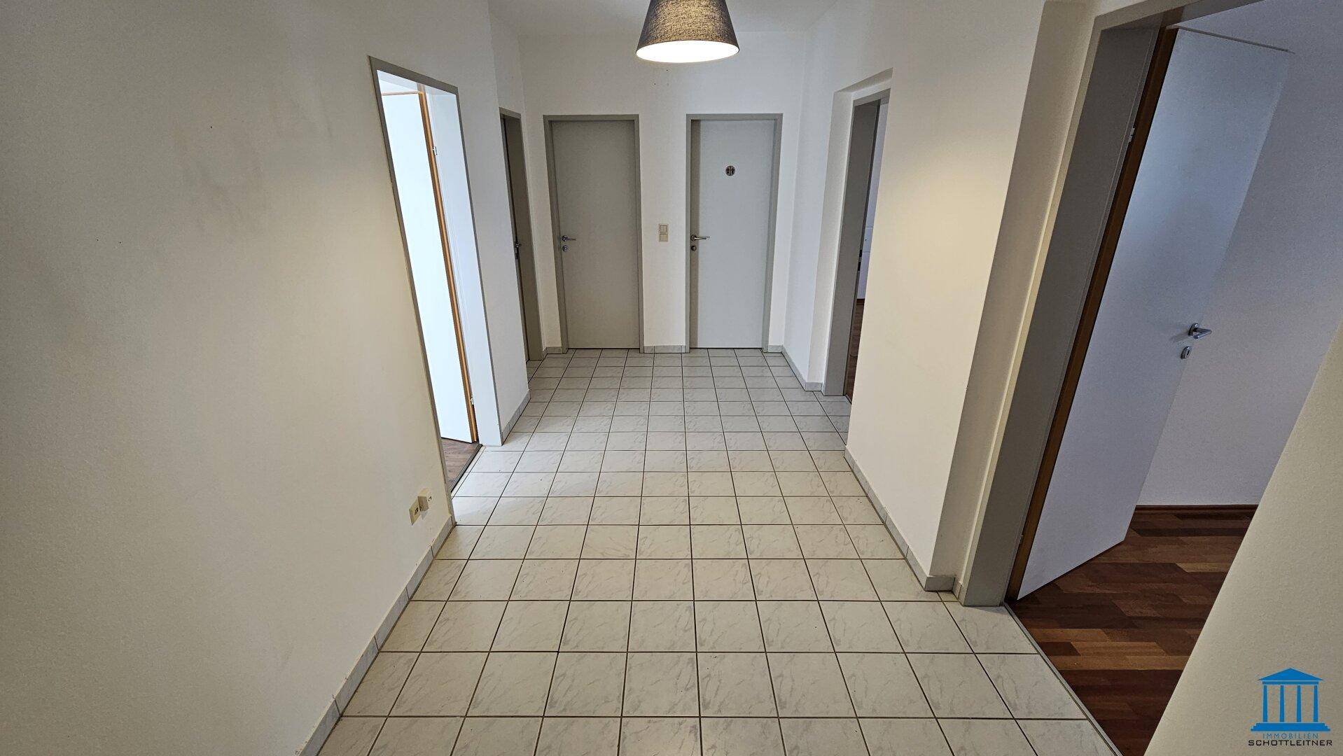 Heller Flur mit Fliesenboden und mehreren Türen, der verschiedene Zimmer verbindet.