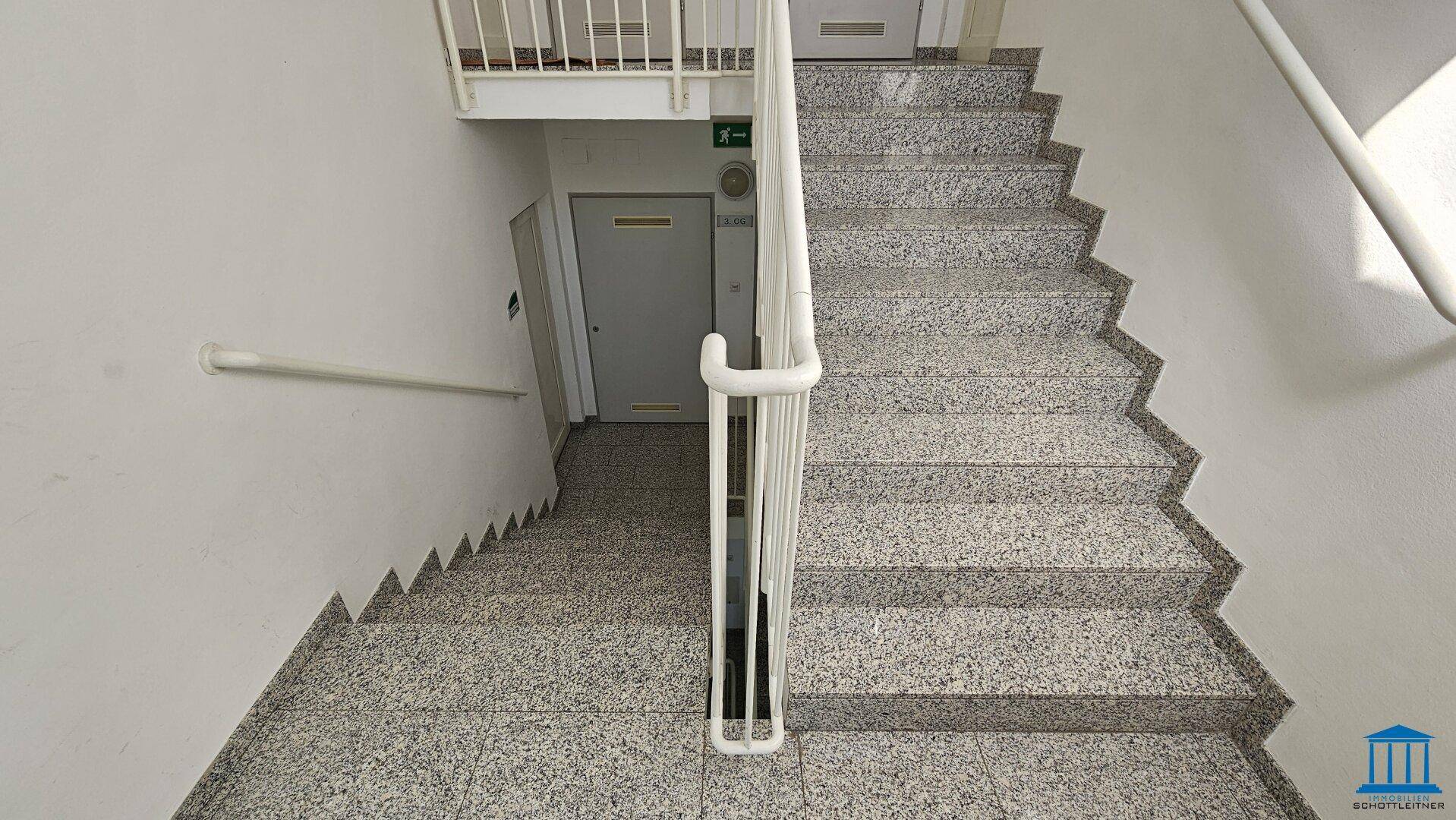 Treppenhaus mit Terrazzoboden und weißen Geländern, verbindet die verschiedenen Stockwerke.