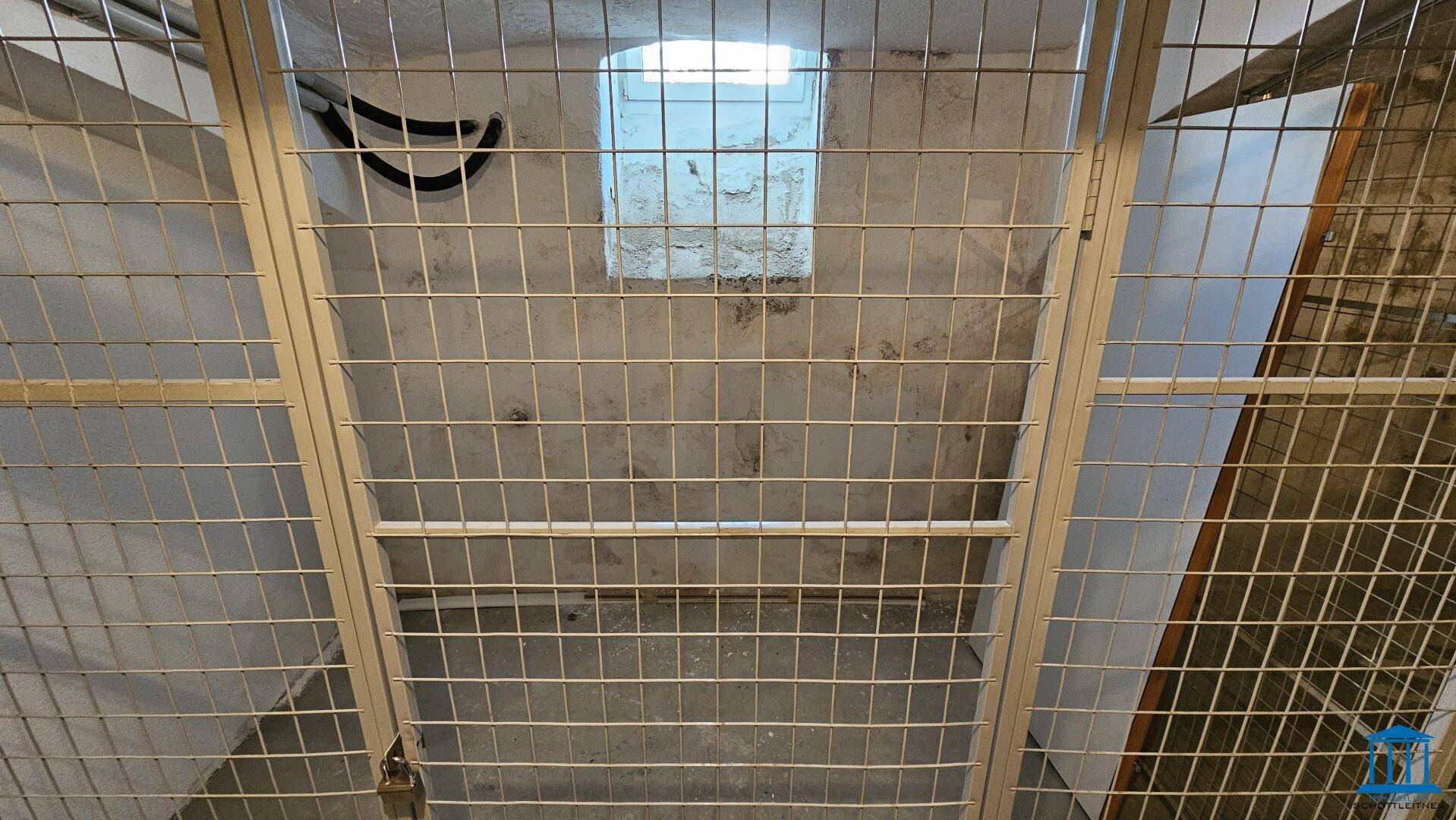 Kellerabteil mit Gitterwand und kleinem Fenster, bietet zusätzlichen Stauraum.