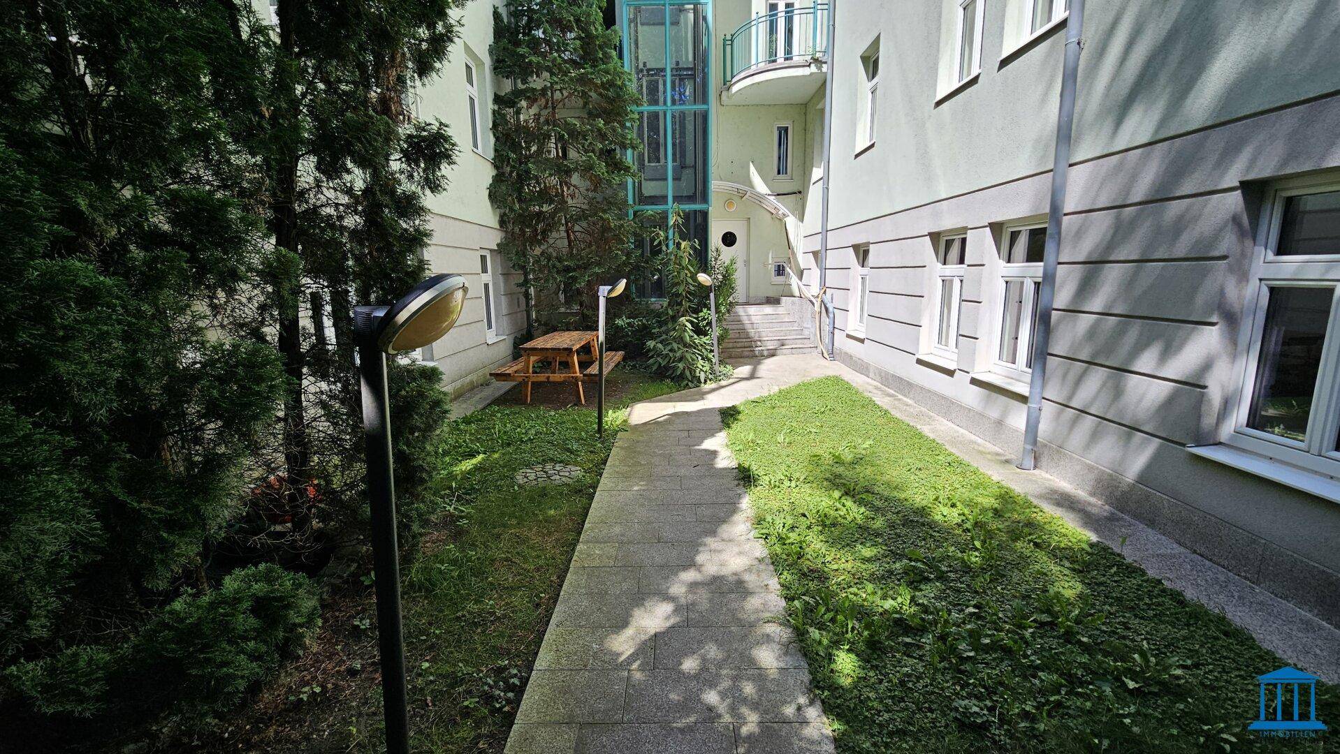 Gepflegter Innenhof mit Sitzgelegenheiten und Zugang zum Gebäude mit Glasaufzug.