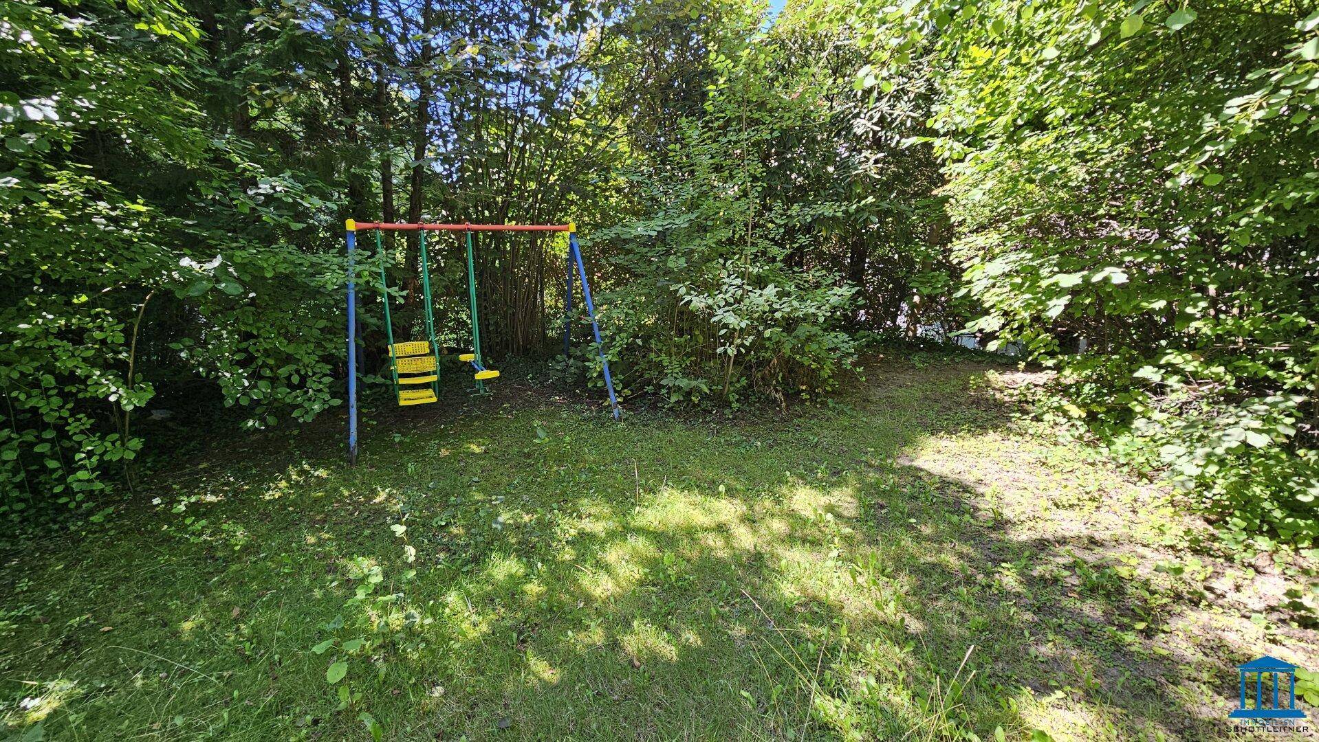 Grüner Gartenbereich mit Schaukel für Kinder, umgeben von Bäumen und Sträuchern.