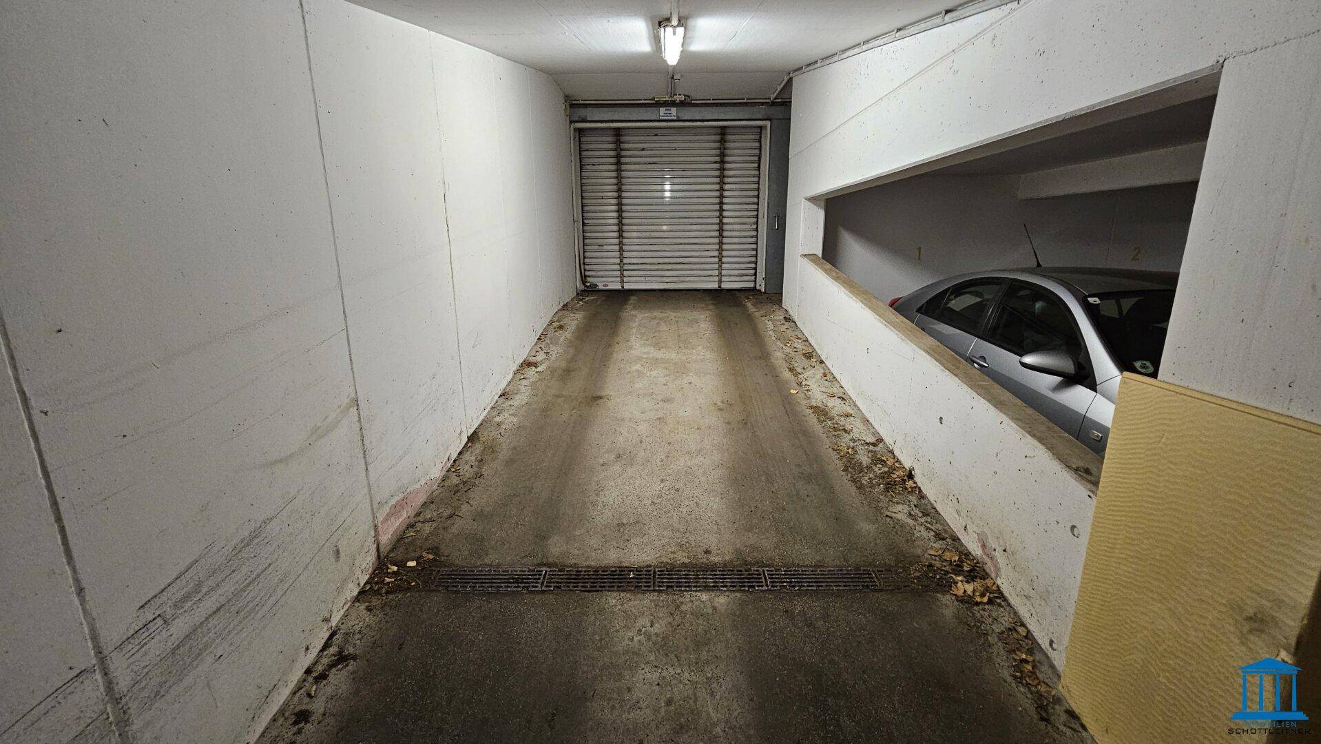 Einfahrt zur Tiefgarage mit Rampe und Rolltor, bietet Zugang zu den Parkplätzen.