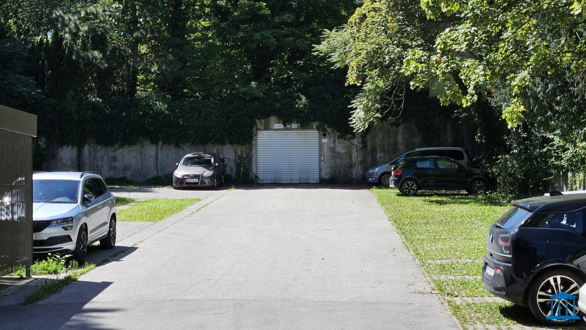 Außenparkplätze und Einfahrt zur Tiefgarage, umgeben von Bäumen und Grünflächen.
