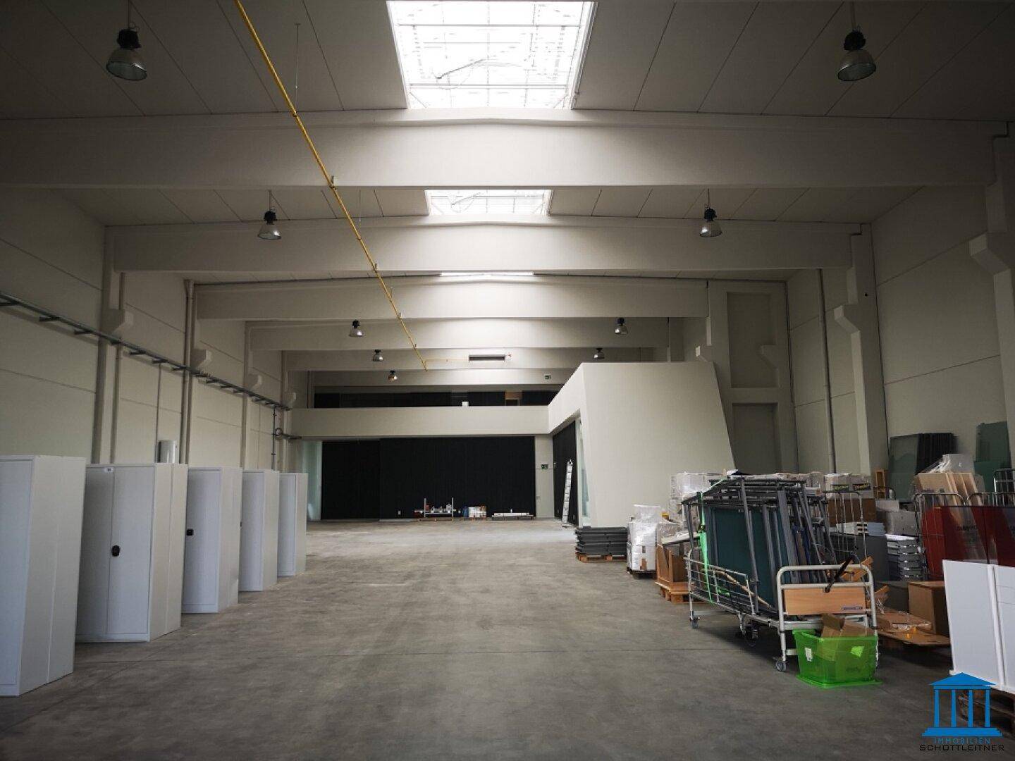 Weitläufige Lagerhalle mit Betonboden, Oberlichtern und industrieller Beleuchtung.
