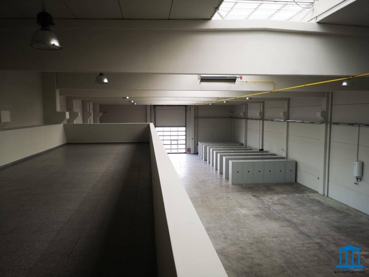 Große Lagerhalle mit Betonboden, Rolltor und einer erhöhten Galerie oder Zwischenebene.