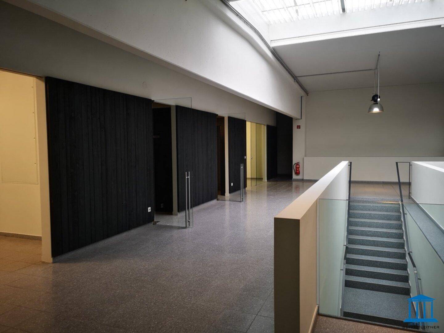 Heller Flur mit Treppenaufgang, Glasgeländer und Zugang zu mehreren Räumen.