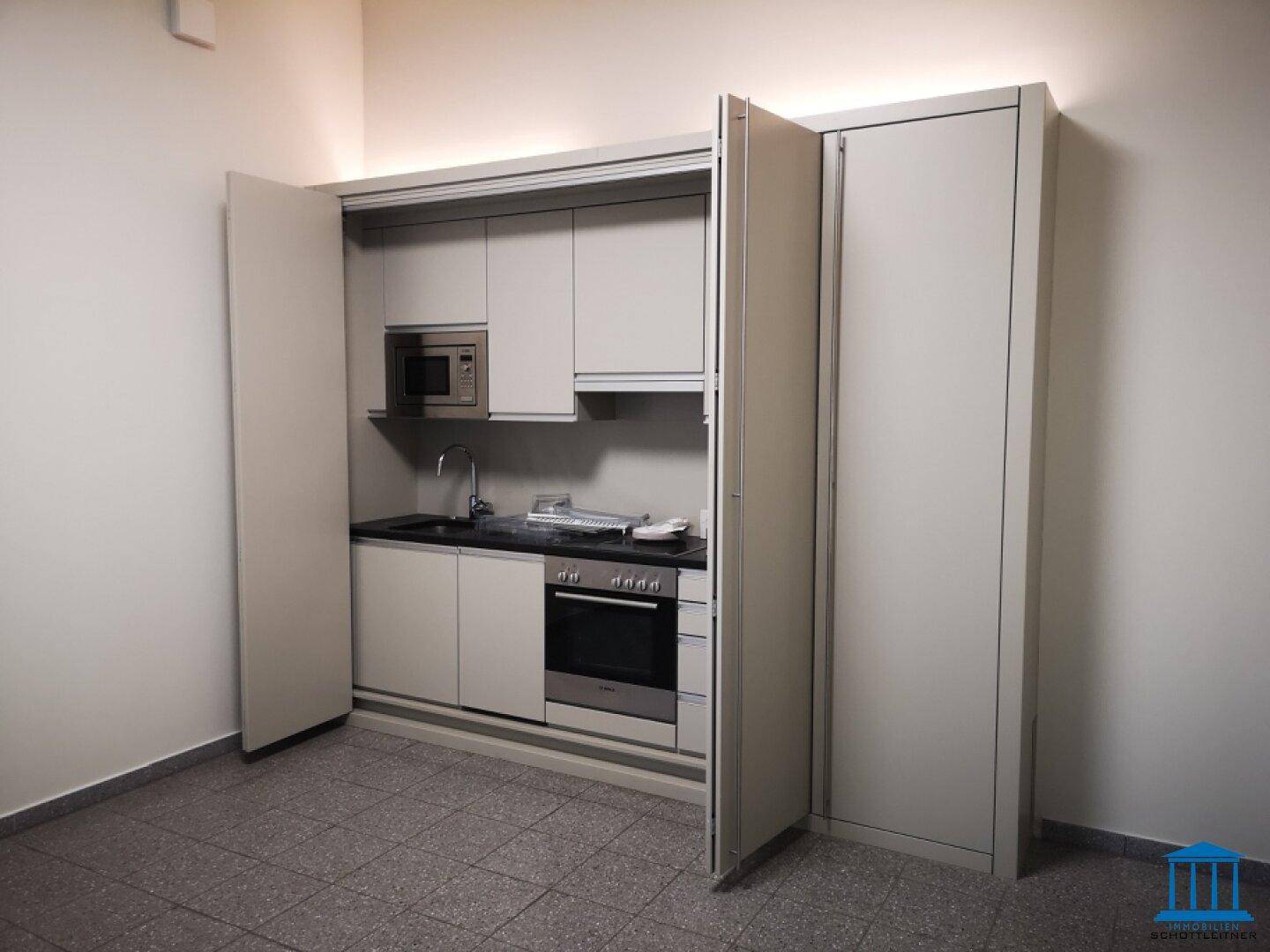 Kompakte Einbauküche mit Mikrowelle, Backofen und Spüle, ideal für kleine Räume.