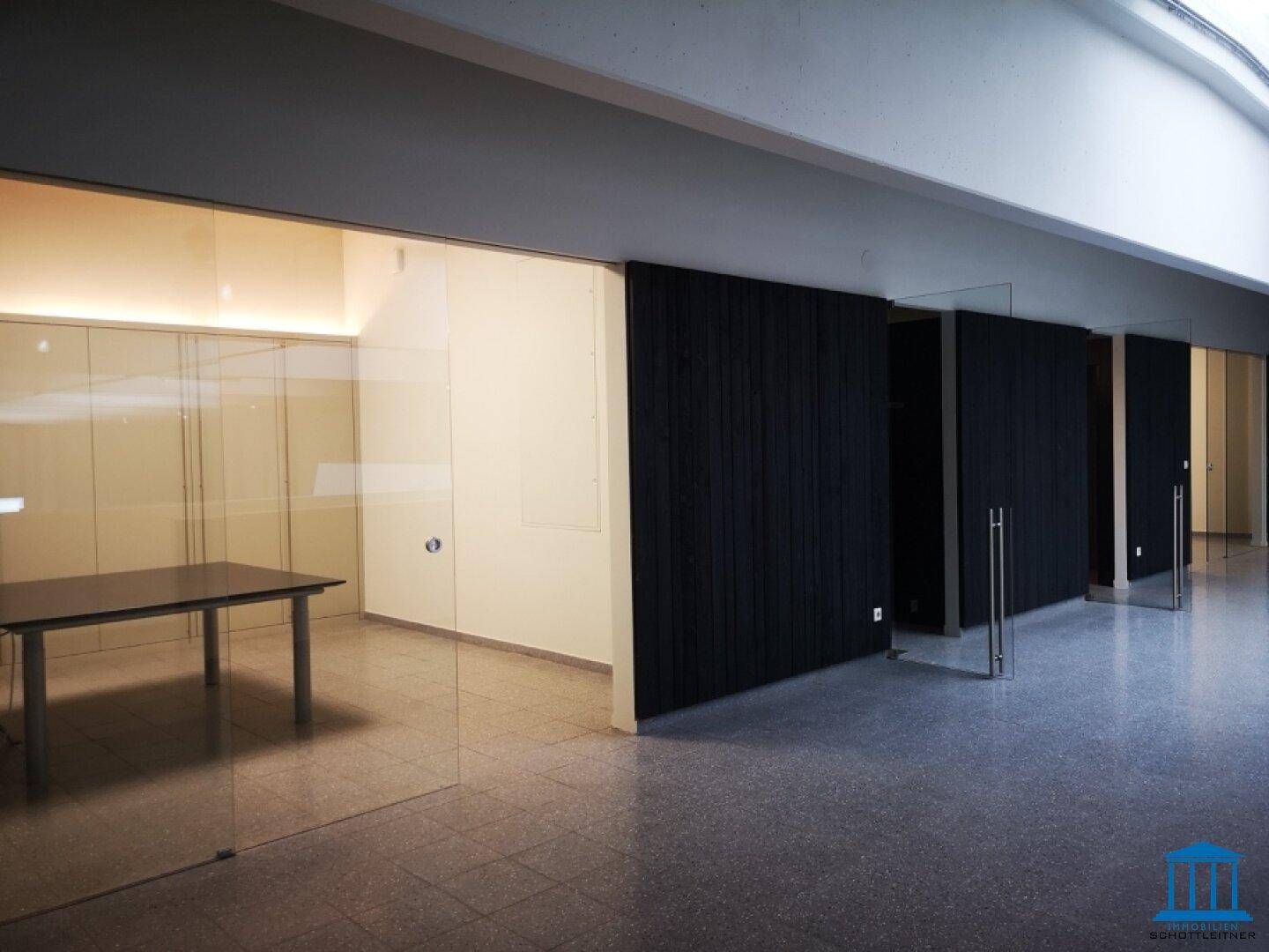 Moderner Bürobereich mit Glastüren, großem Tisch und Terrazzoboden.