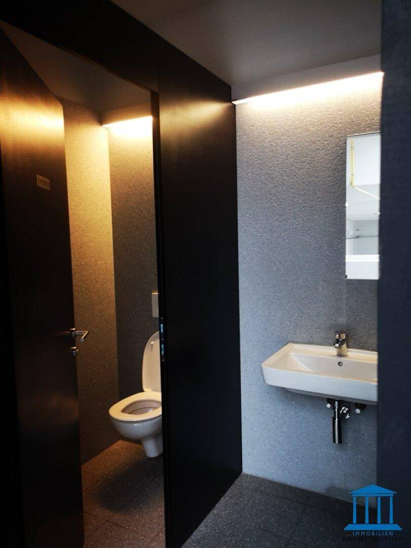 Moderne Toilette mit Waschbecken und indirekter Beleuchtung, in dunklem Design.