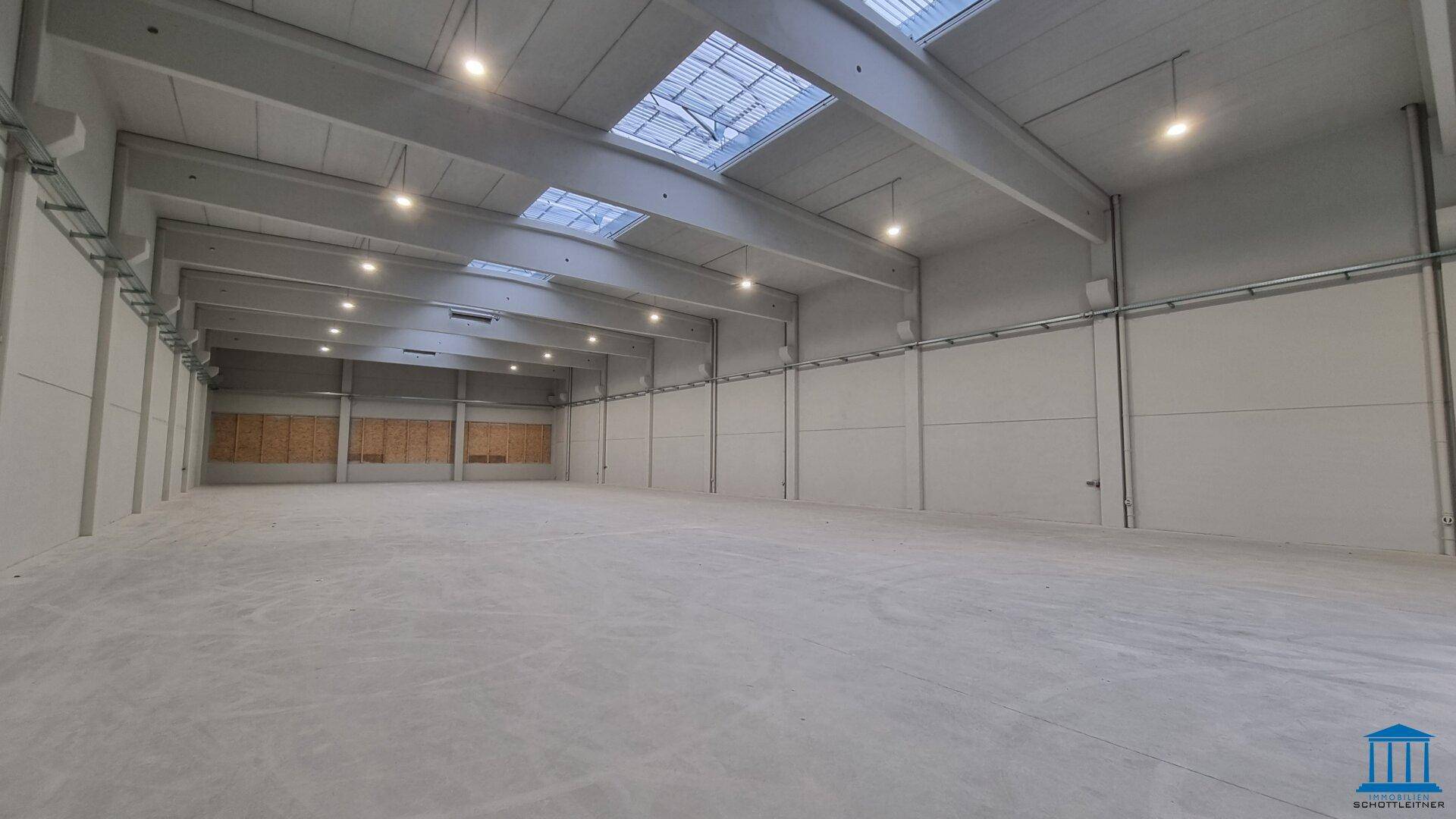 Große, leere Industriehalle mit hohen Decken, Betonboden und Oberlichtern für viel Tageslicht.