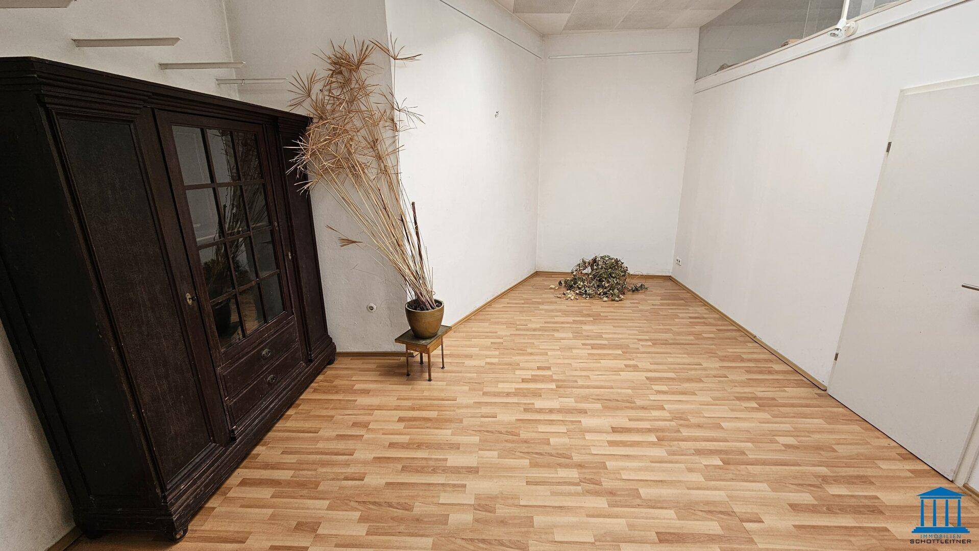 Weiterer Bereich des Gewerberaums mit Laminatboden, einem antiken Schrank und minimalistischer Dekoration.