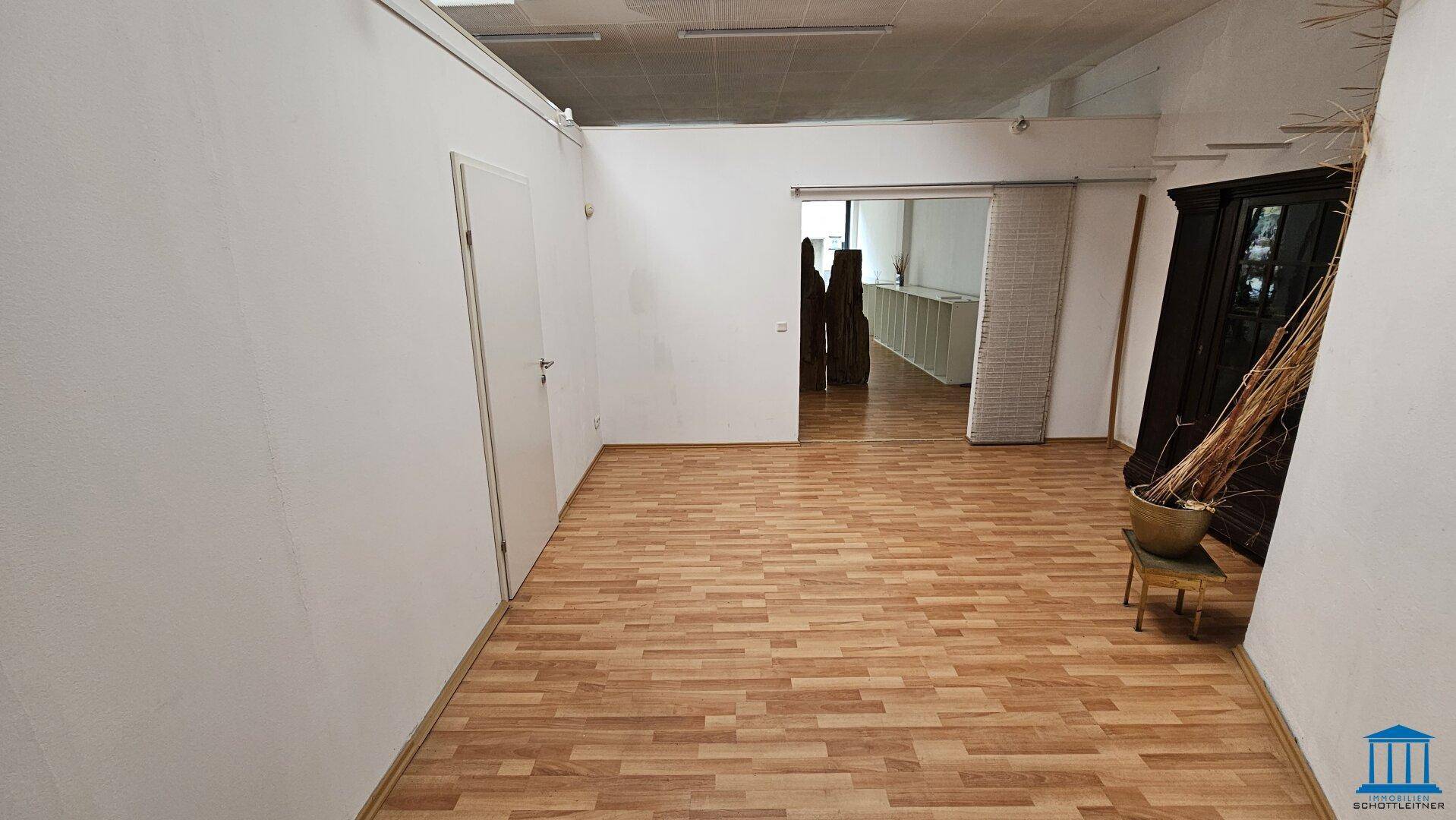 Blick durch den Gewerberaum mit Laminatboden, weißen Wänden und einem Durchgang zu einem weiteren Bereich.