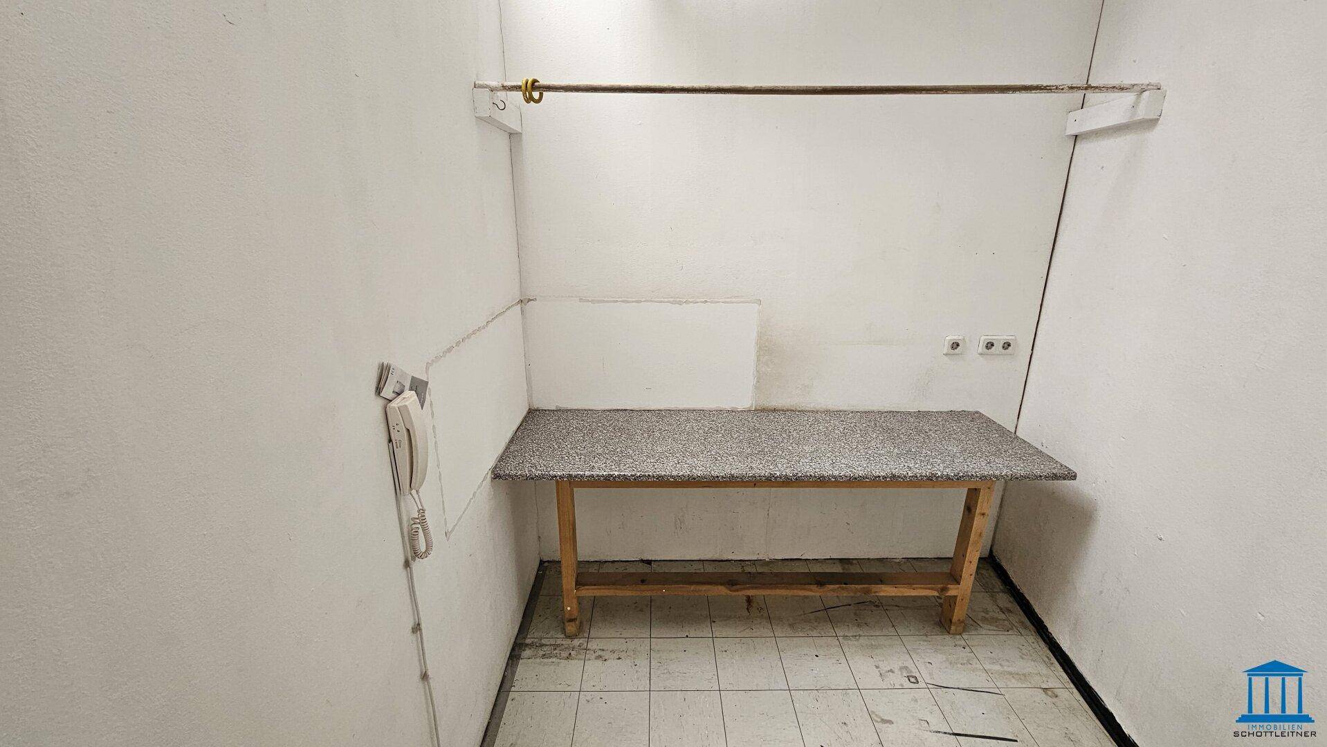 Kleiner Abstellraum mit gefliestem Boden, einer Arbeitsplatte und sichtbaren Steckdosen.