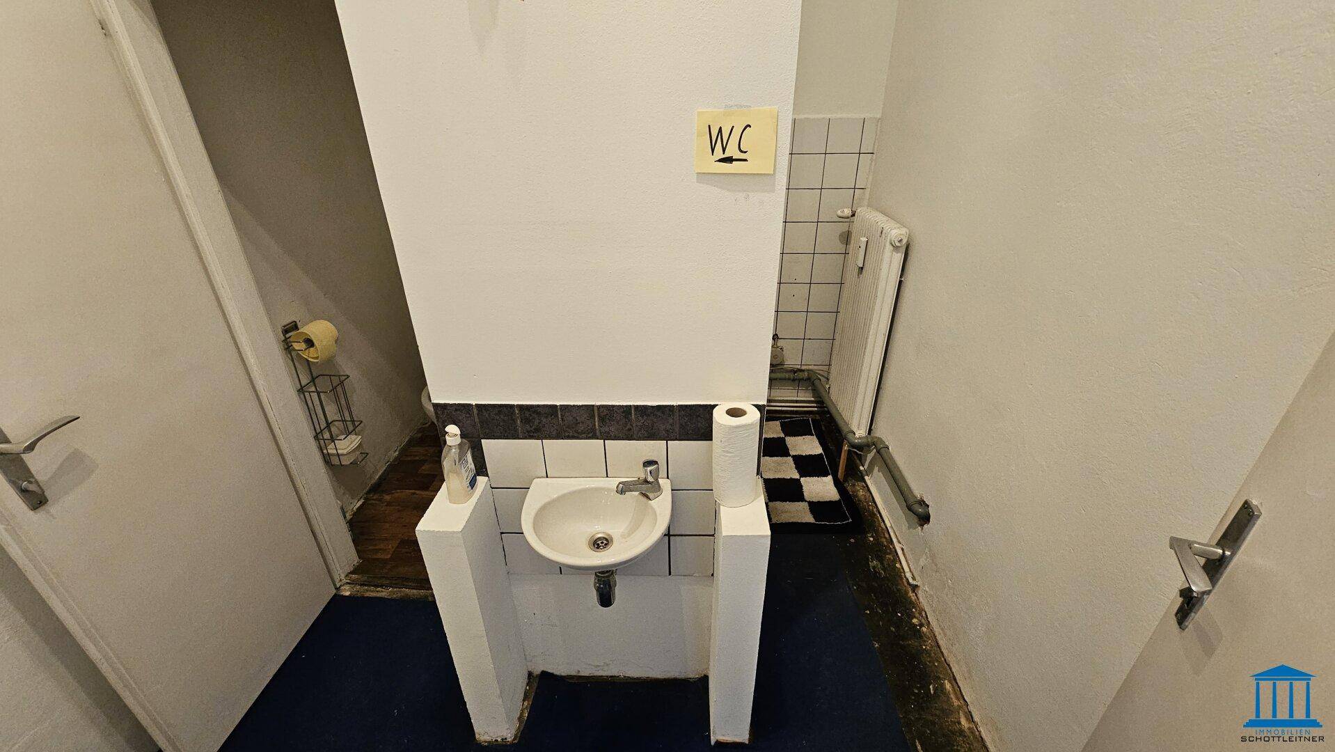 Einfache Gästetoilette mit kleinem Waschbecken, Fliesen und einem schwarz-weiß karierten Boden.
