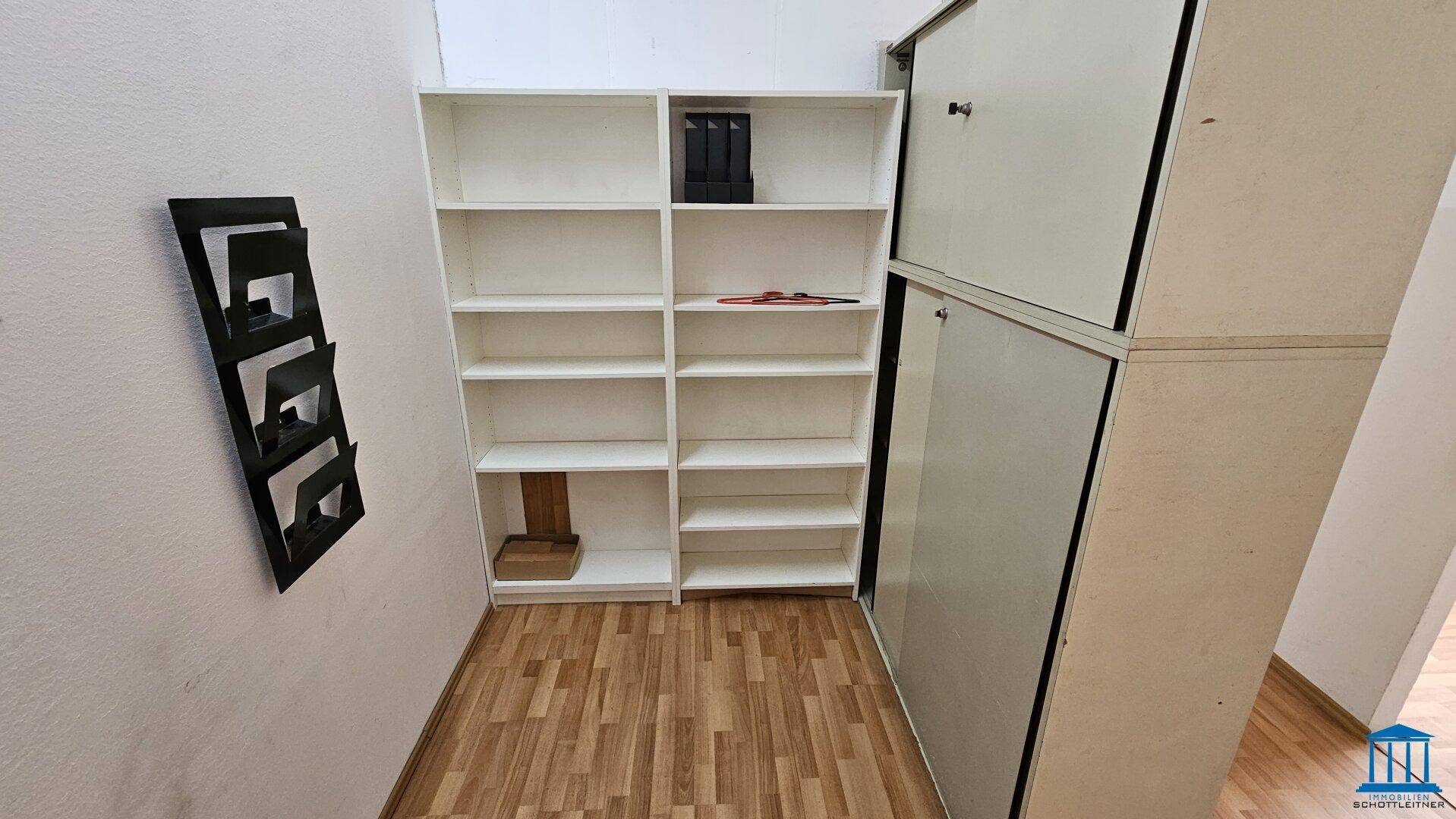 Schmaler Lagerbereich mit weißen Regalen und einem Schrank, ausgestattet mit Laminatboden.