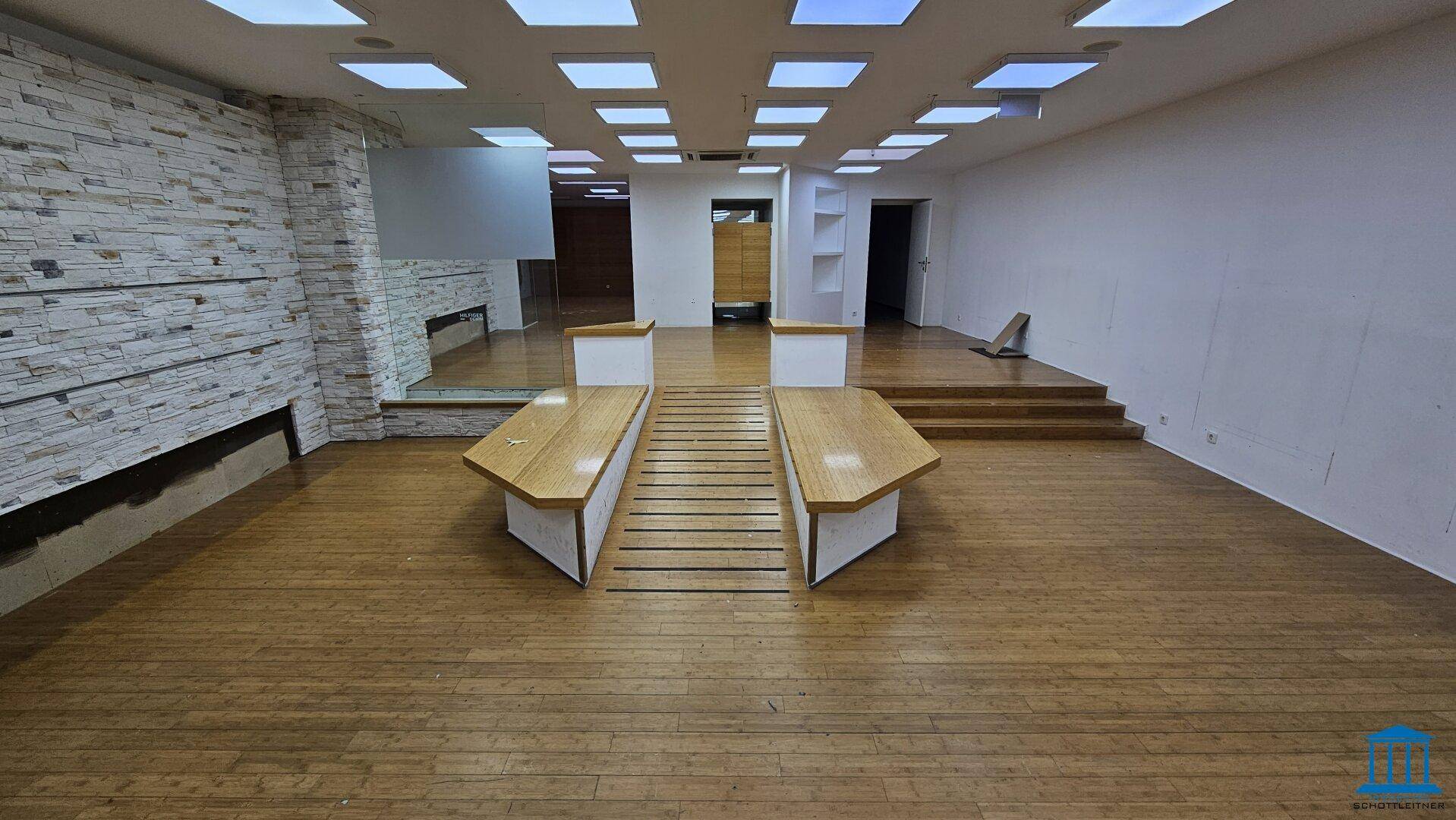 Weitläufiger Verkaufsraum mit Holzdielenboden, Stufen und modernen Präsentationsmöbeln aus Holz.