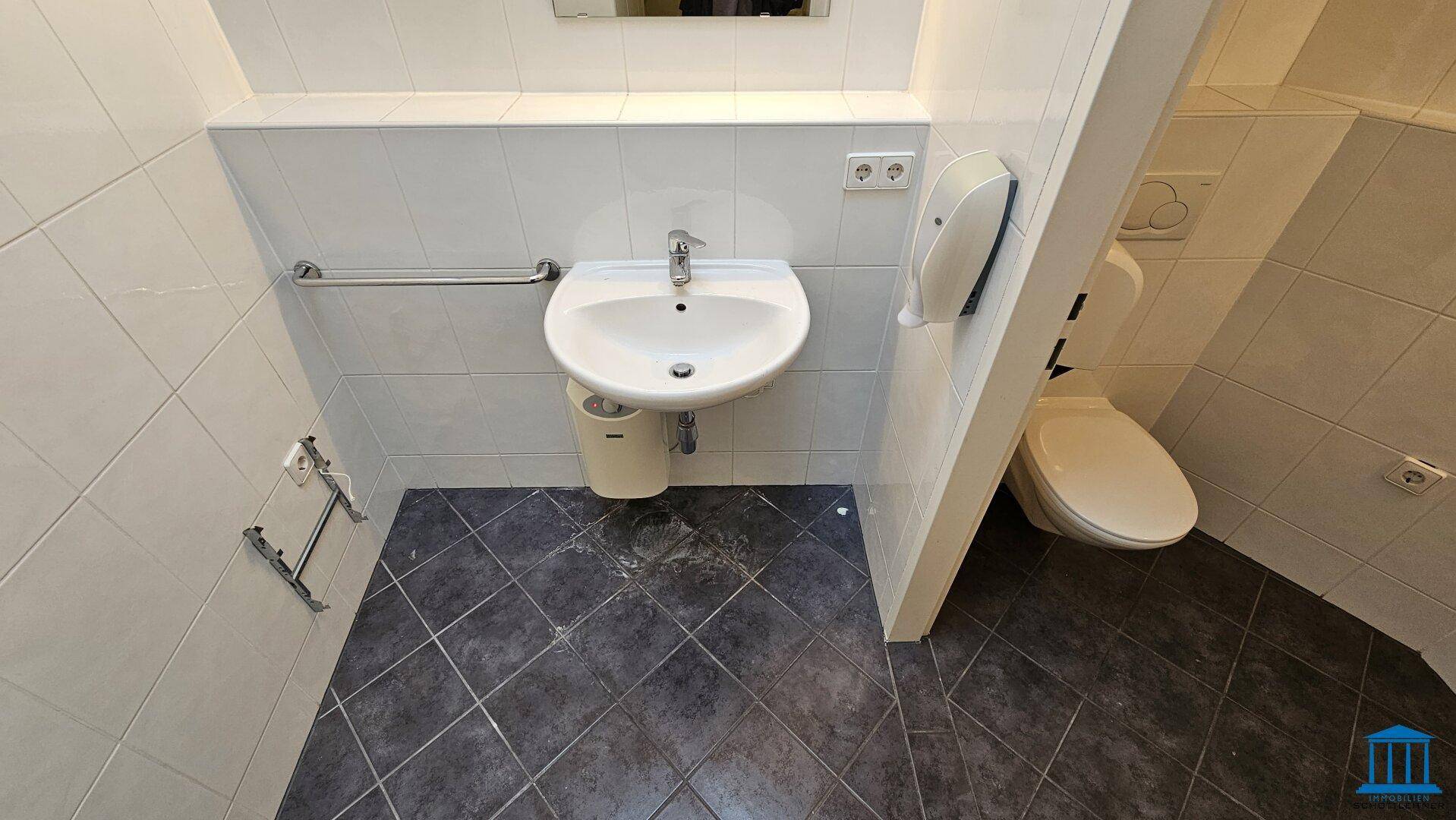 Funktionale Toilette mit Waschbecken, Wand-WC und dunklen Fliesen auf dem Boden.