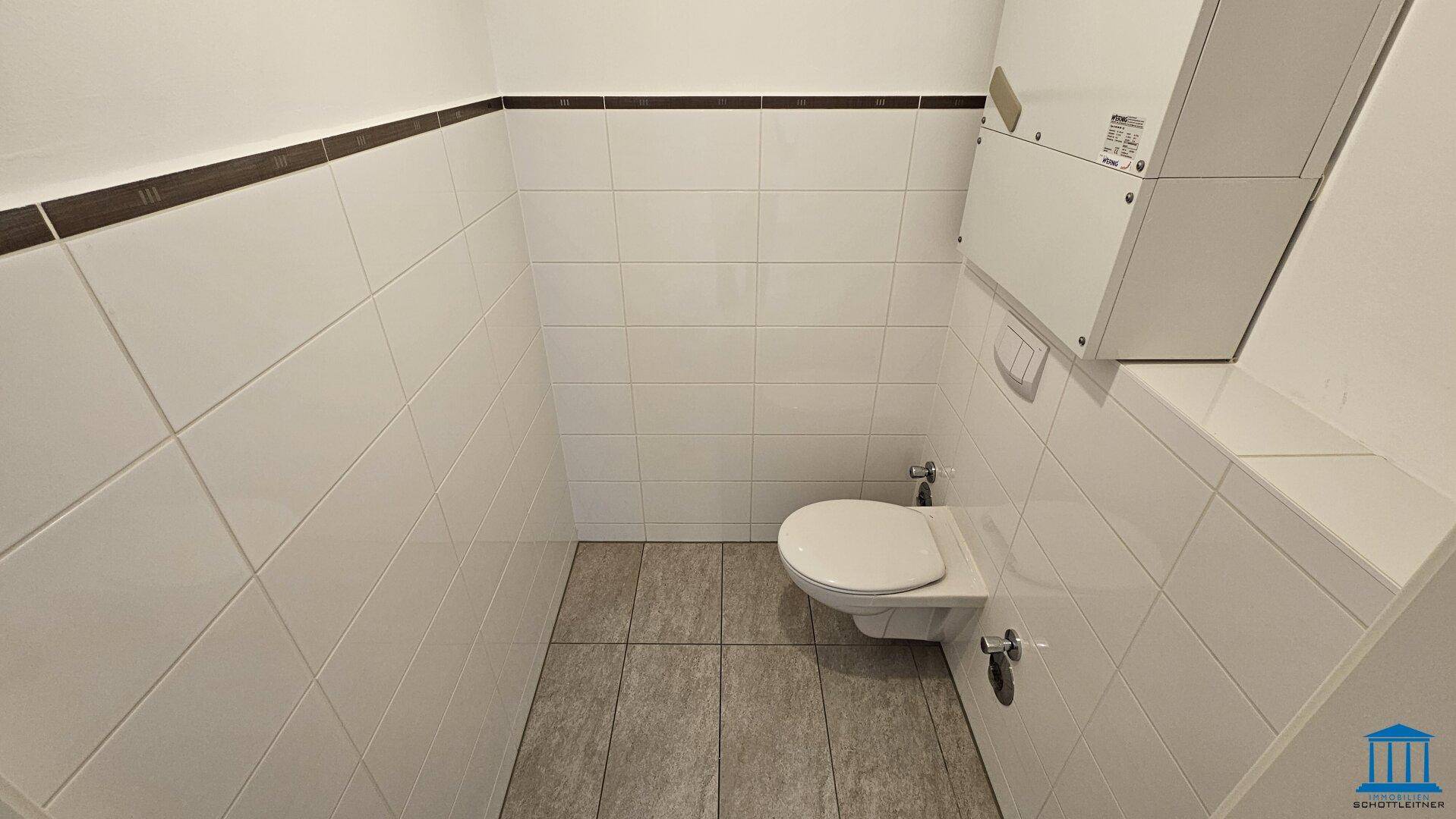 Separate Toilette mit Wand-WC und weißen Fliesen, sauber und funktional.