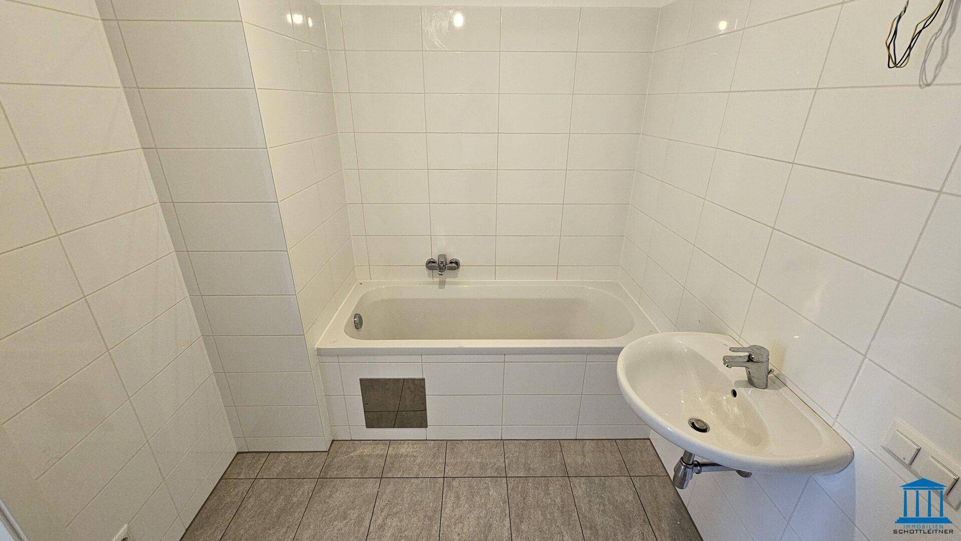 Badezimmer mit Badewanne, Waschbecken und weißen Wandfliesen, bereit zur Nutzung.