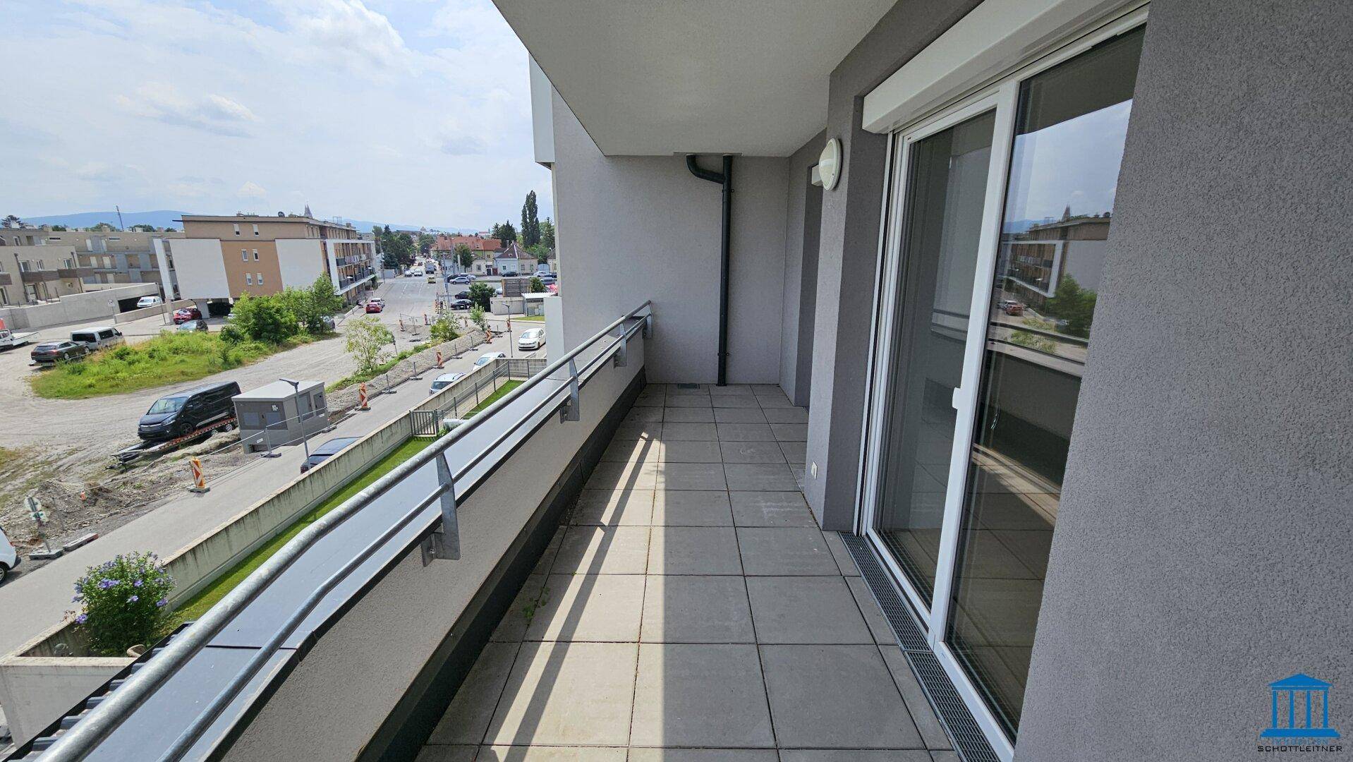 Langer Balkon mit Fliesenboden und Blick auf die umliegende Bebauung und Straße.