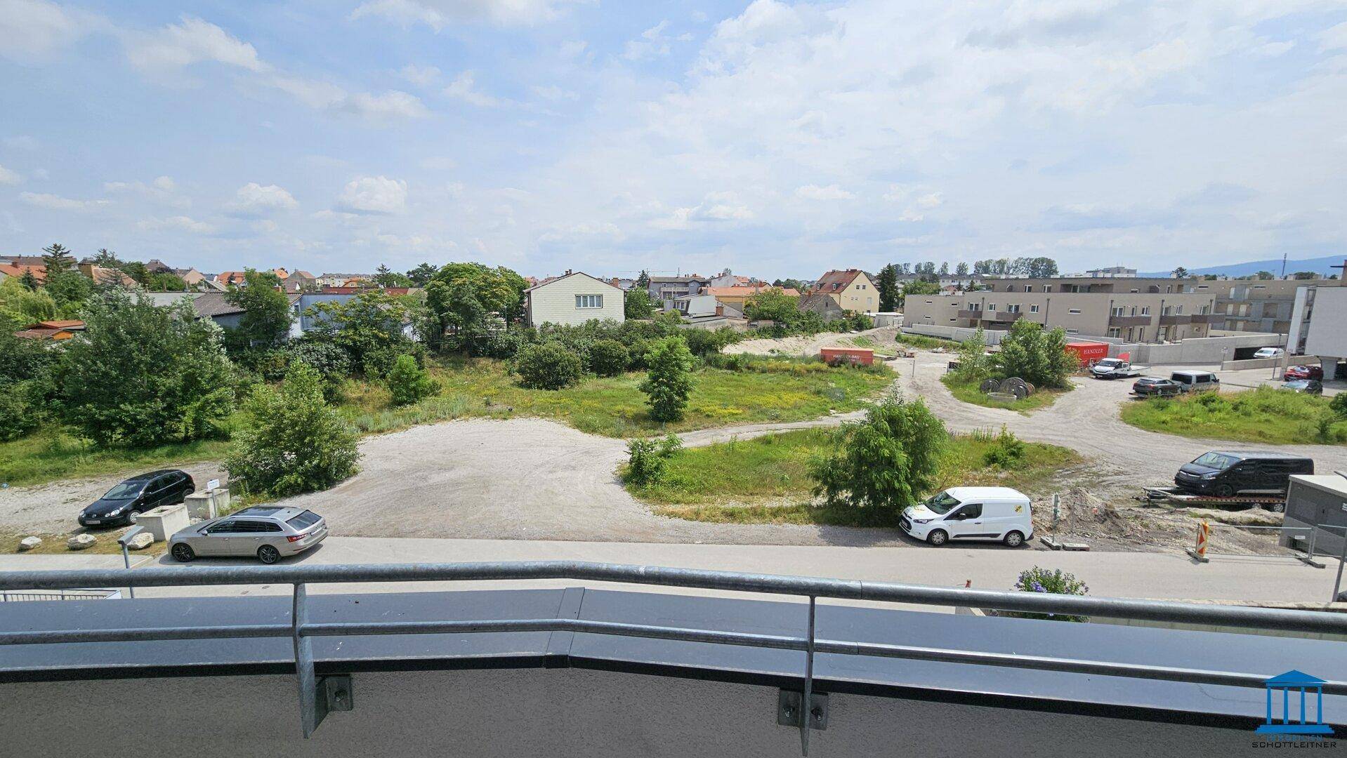 Weitläufiger Blick über grüne Flächen und die umliegende Wohnbebauung unter blauem Himmel.