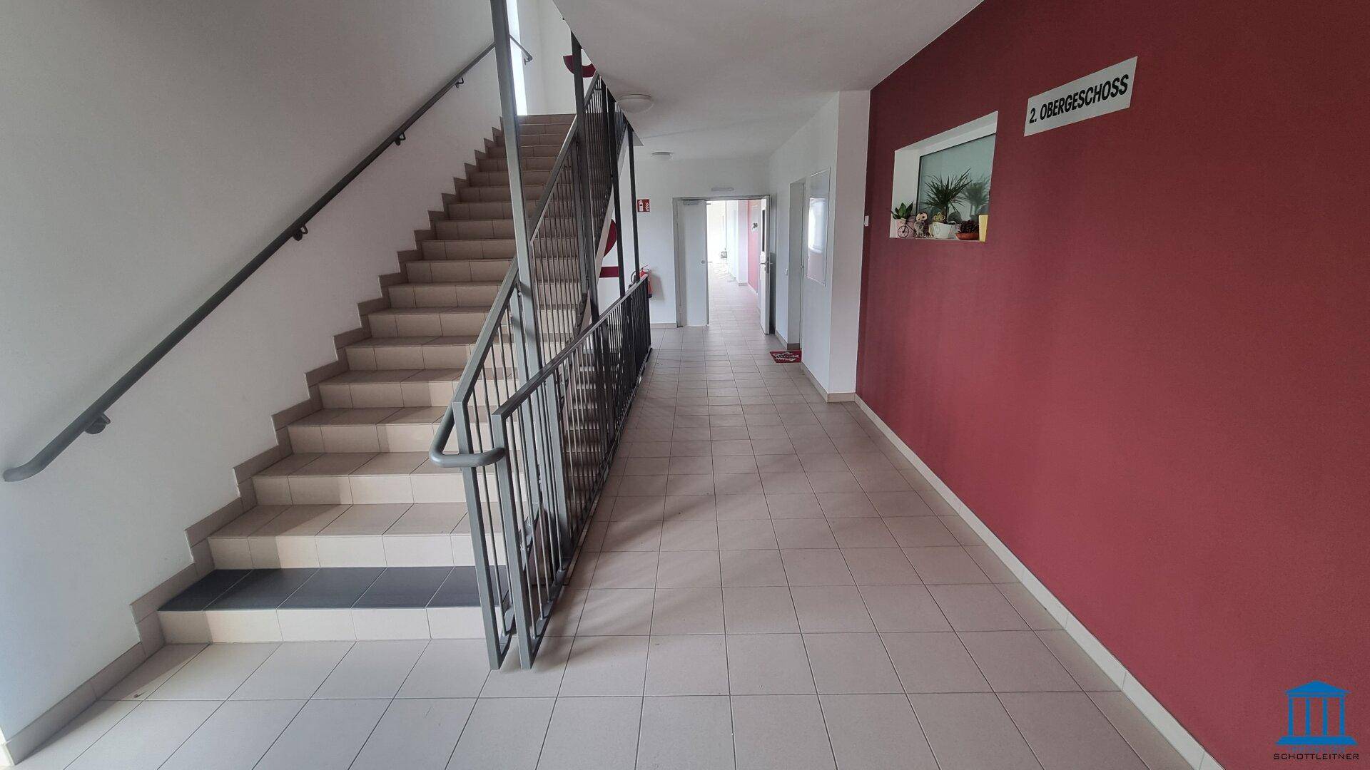 Geräumiges Treppenhaus mit Fliesenboden und Geländer, führt zu den oberen Stockwerken.