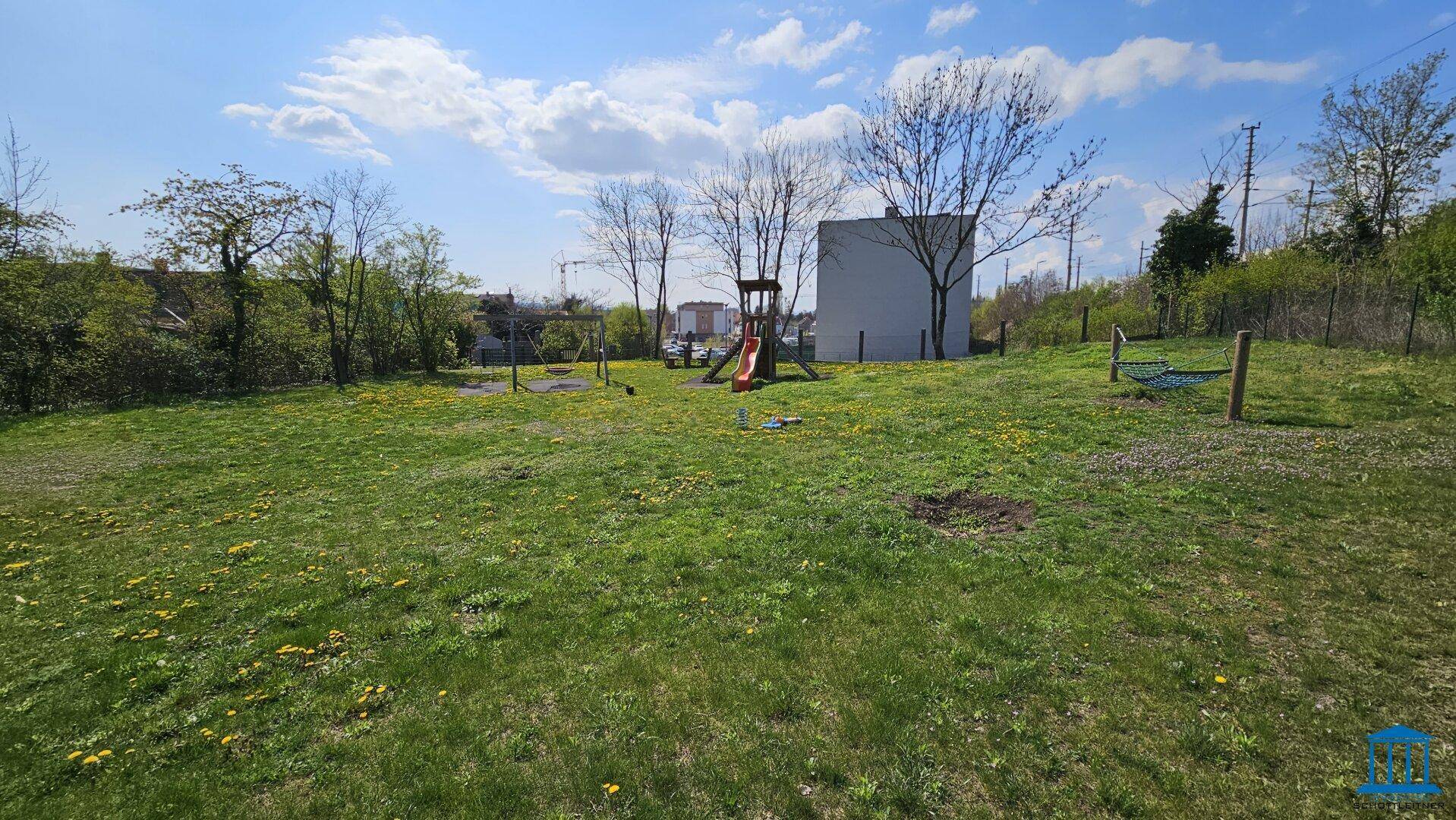 Großer Gartenbereich mit Spielplatz und Hängematte unter blauem Himmel, ideal für Familien.
