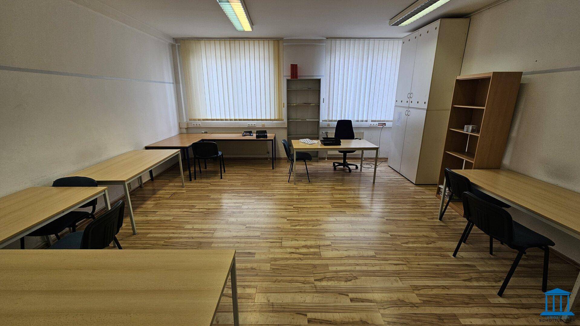 Großer Büroraum mit verschiedenen Schreibtischkonfigurationen, Regalen und hellem Laminatboden, geeignet für flexible Nutzung.