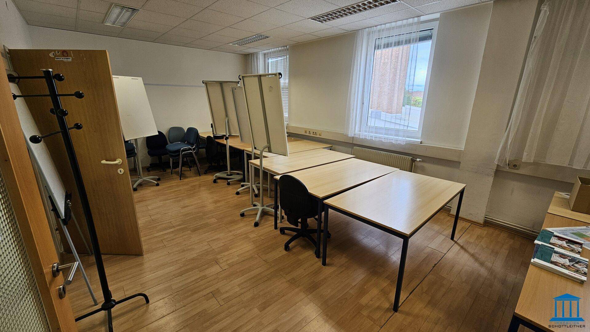 Kursraum mit Holzboden, Tischen und Stühlen, sowie mehreren Whiteboards und einem Fenster.