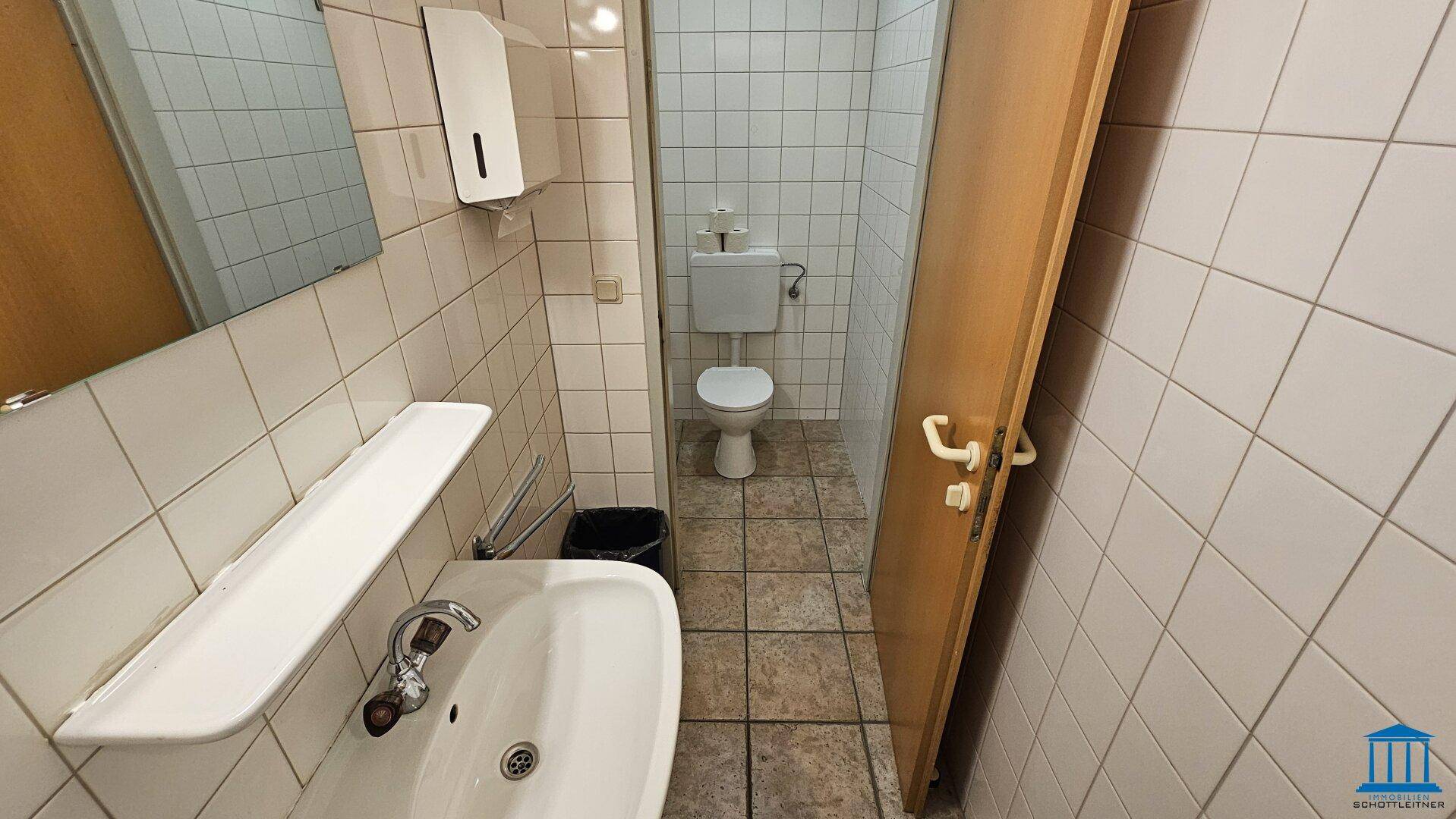 Funktionales Badezimmer mit Waschbecken und Toilette, ausgestattet mit weißen Fliesen.