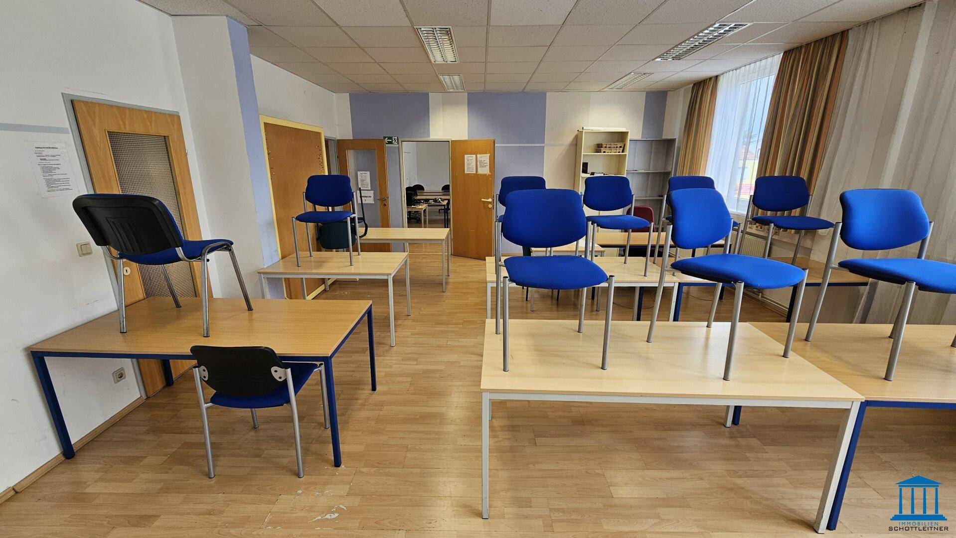 Großer Konferenzraum mit Tischen und blauen Stühlen, ideal für Seminare und Workshops.