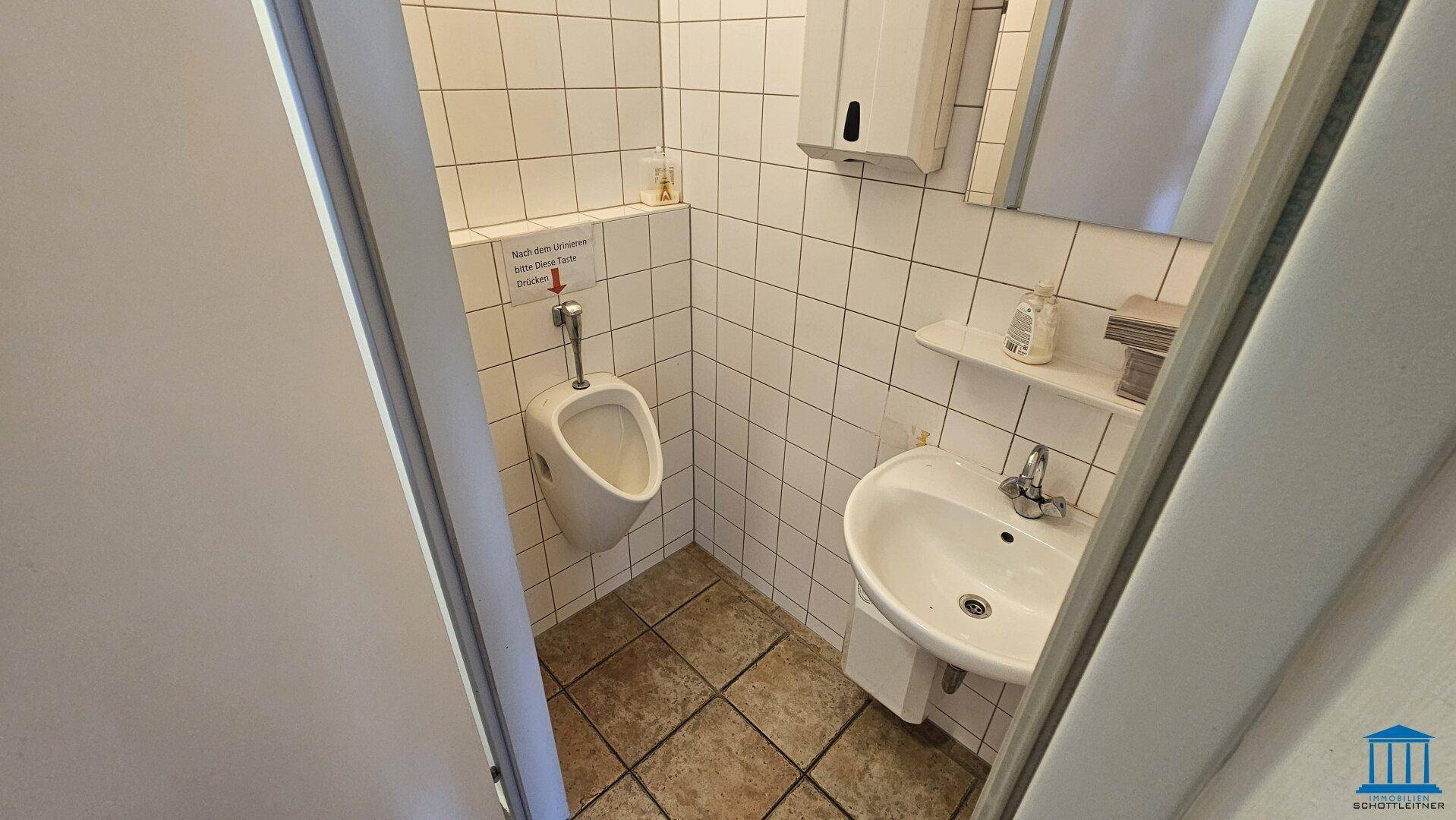 Herren-WC mit Urinal, Waschbecken und weißen Fliesen, sauber und gepflegt.