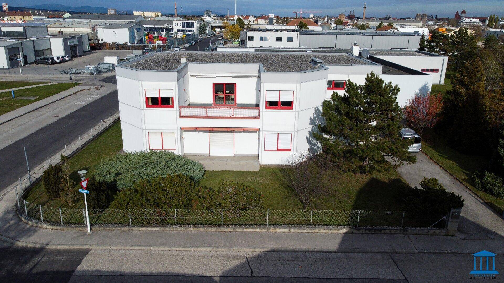 Frontansicht des Bürogebäudes von oben mit roten Fensterrahmen und umliegender Grünfläche an einem sonnigen Tag.