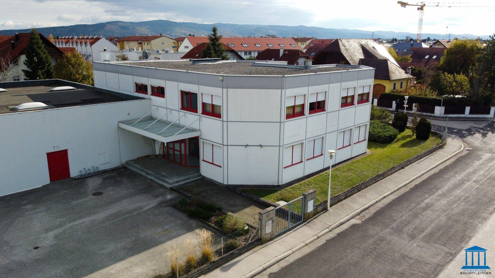 Luftaufnahme des Haupteingangs des Bürogebäudes mit Vordach und gepflegter Außenanlage unter blauem Himmel.