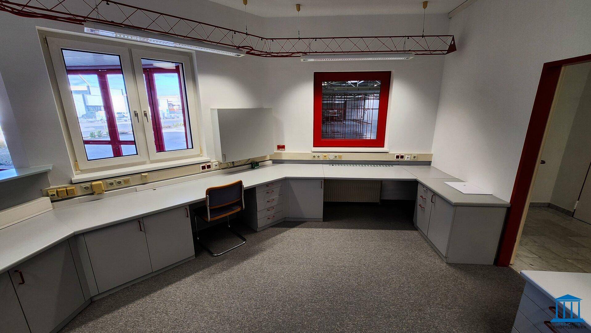 Büro mit großem Fenster, U-förmigem Schreibtisch und Blick auf die Umgebung, gut beleuchtet.