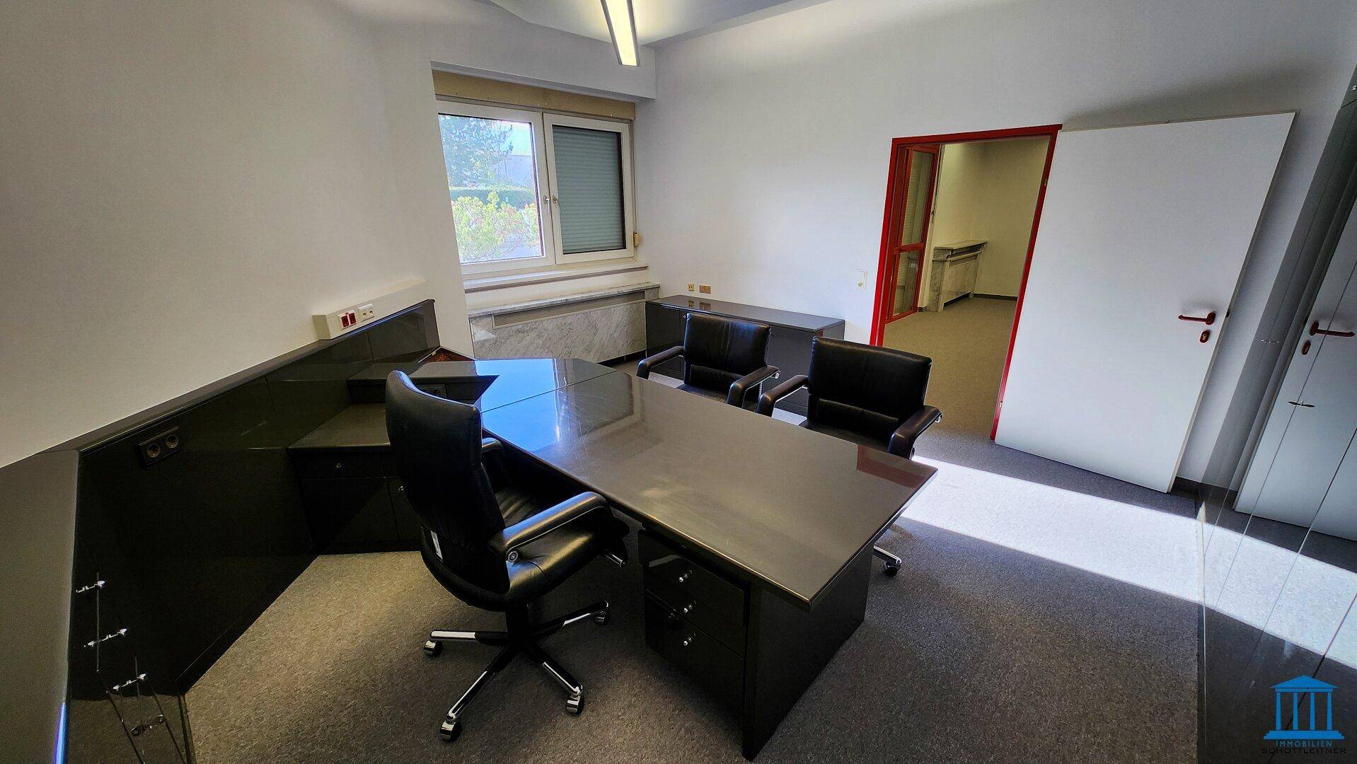 Chefbüro mit großem Schreibtisch, Bürostühlen und Fenster mit Blick ins Grüne, hell und geräumig.