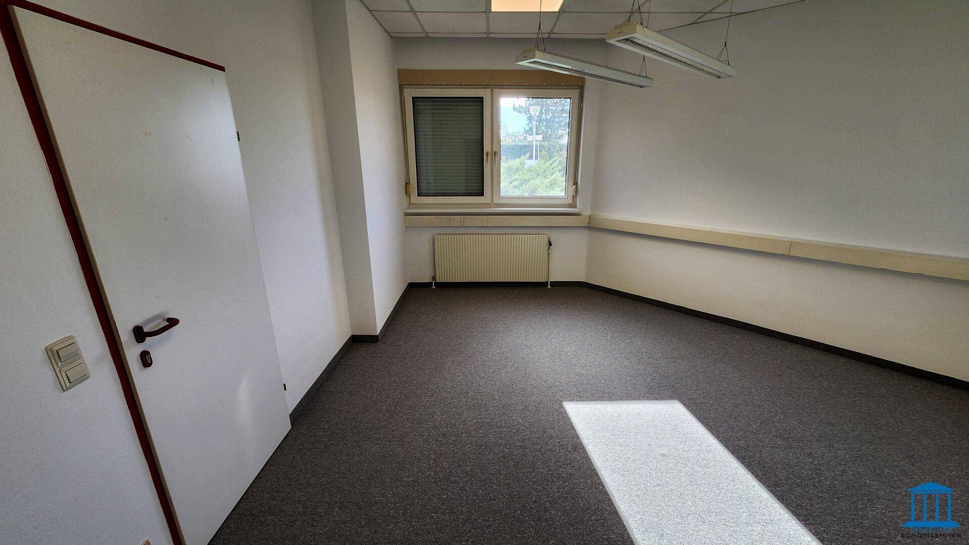 Leeres Büro mit Teppichboden, Fenster und Heizkörper, bereit zur individuellen Gestaltung.