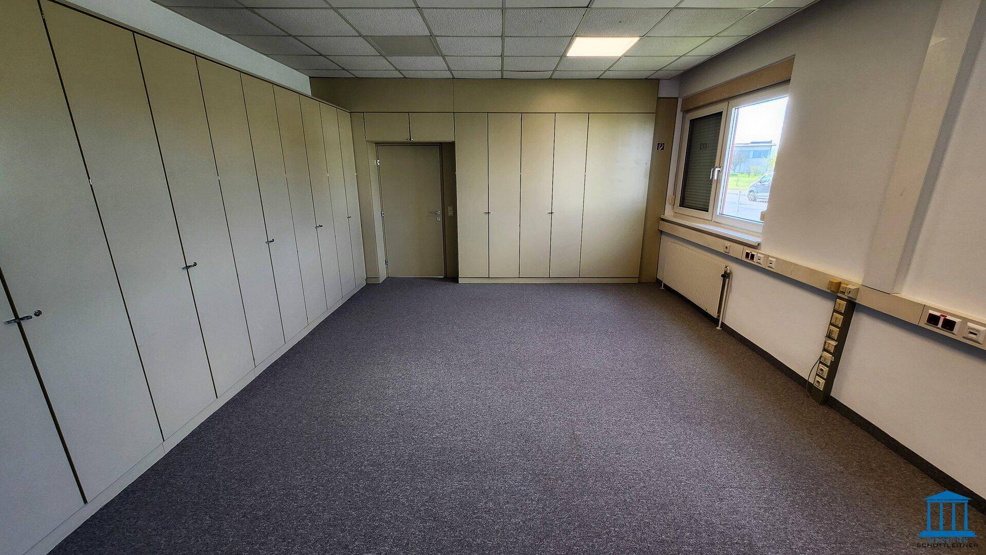 Büro mit Teppichboden, Einbauschränken und Tür zu einem weiteren Raum, funktional und hell.
