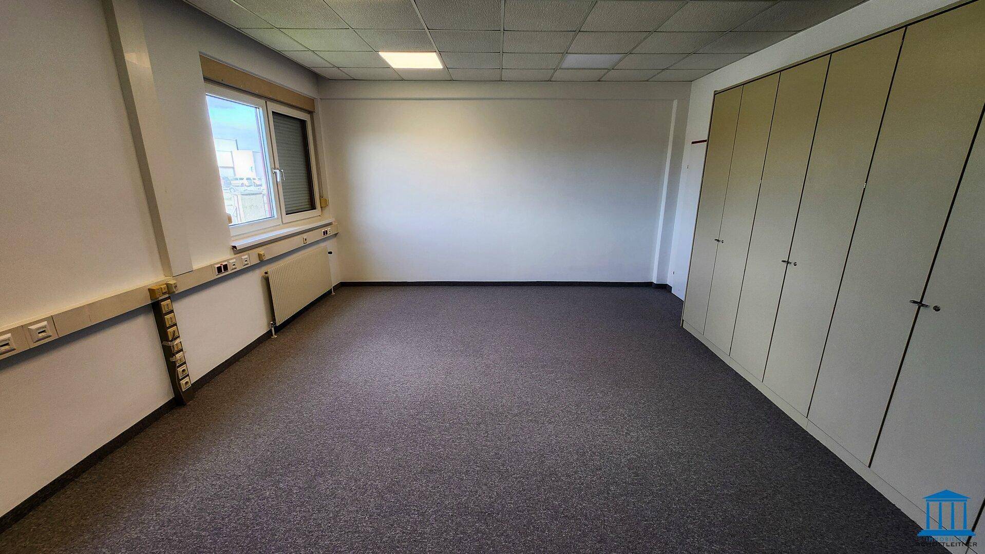 Geräumiges Büro mit Teppichboden und einer langen Reihe von Einbauschränken entlang der Wand.