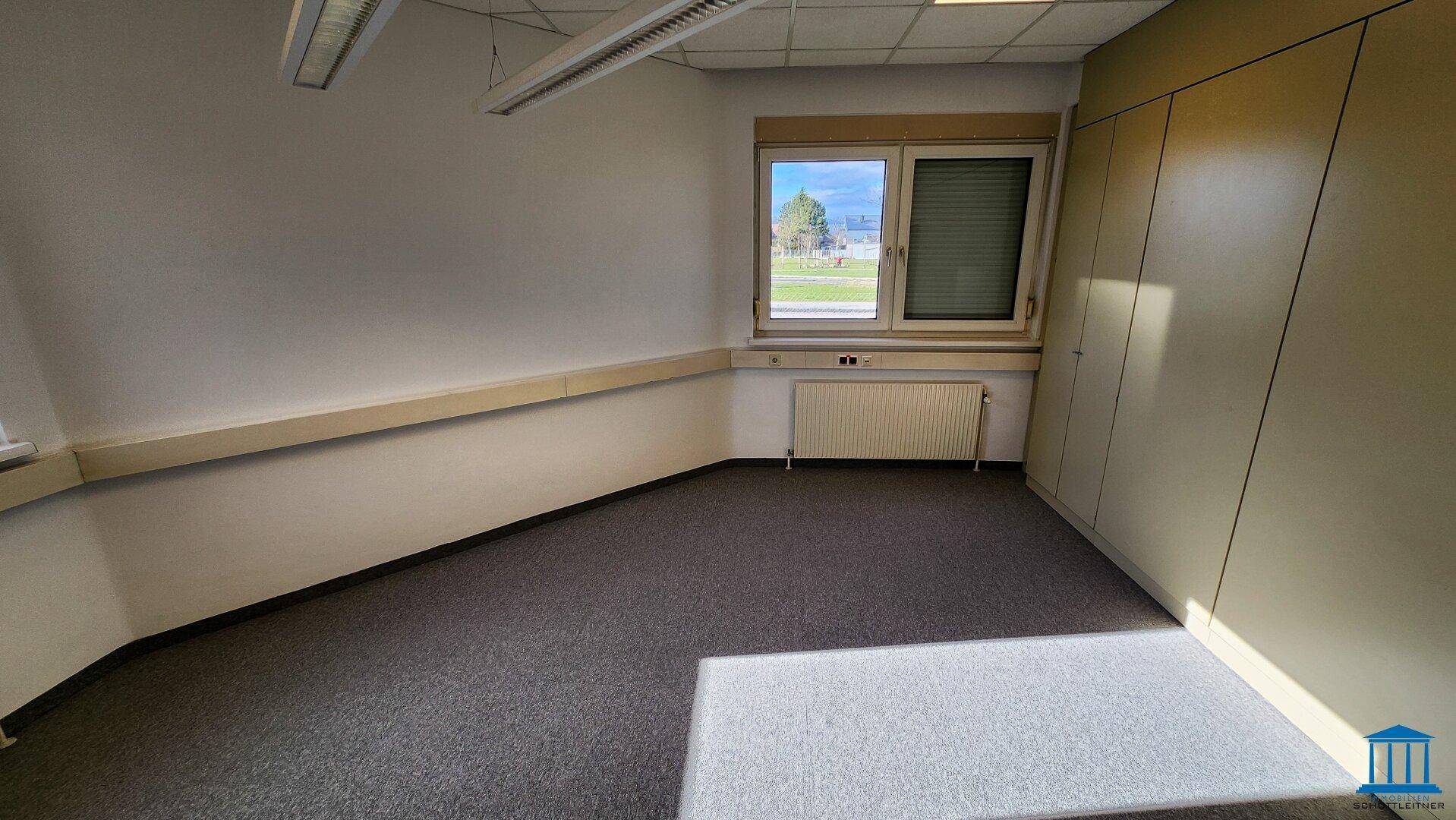 Büro mit Teppichboden, Fenster und integrierten Wandschränken für zusätzlichen Stauraum.