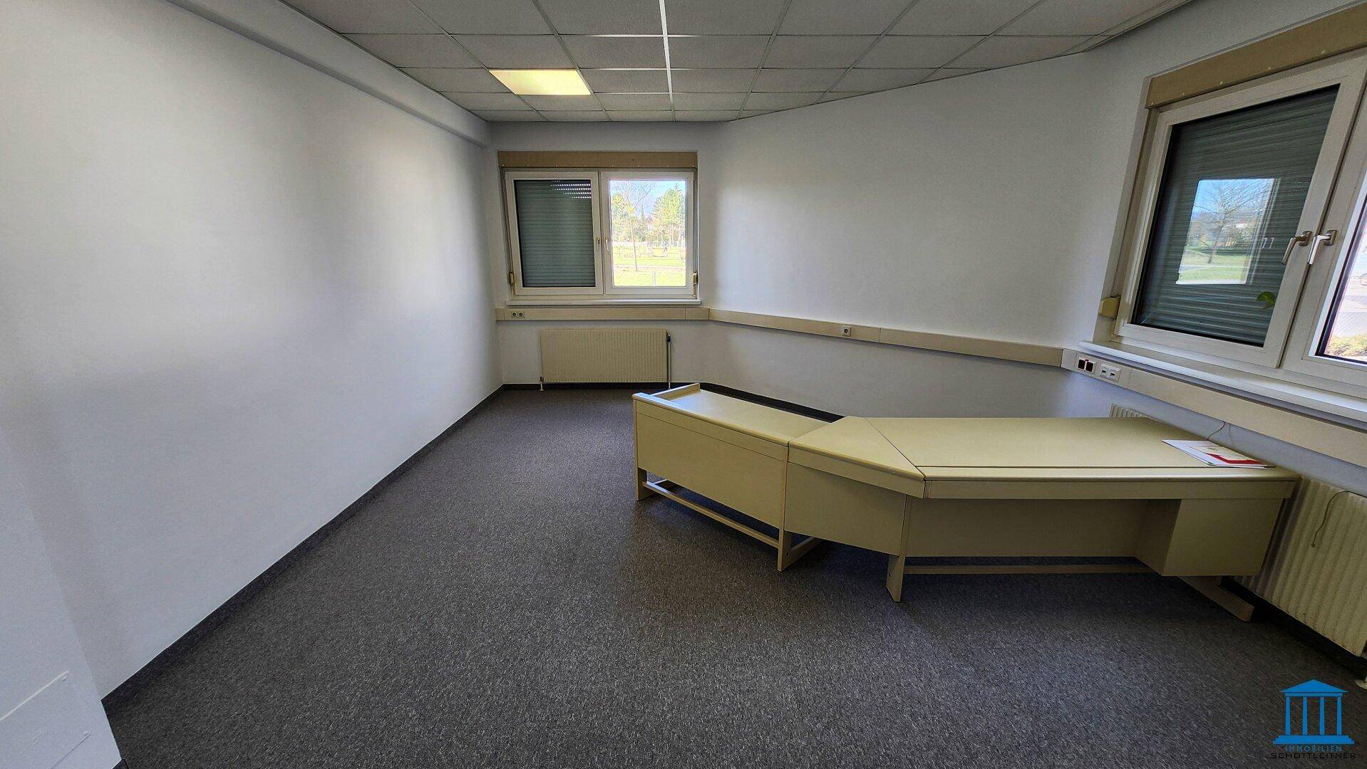 Büro mit Teppichboden, Fenster und einem Eckschreibtisch in heller Farbe, funktional und einladend.