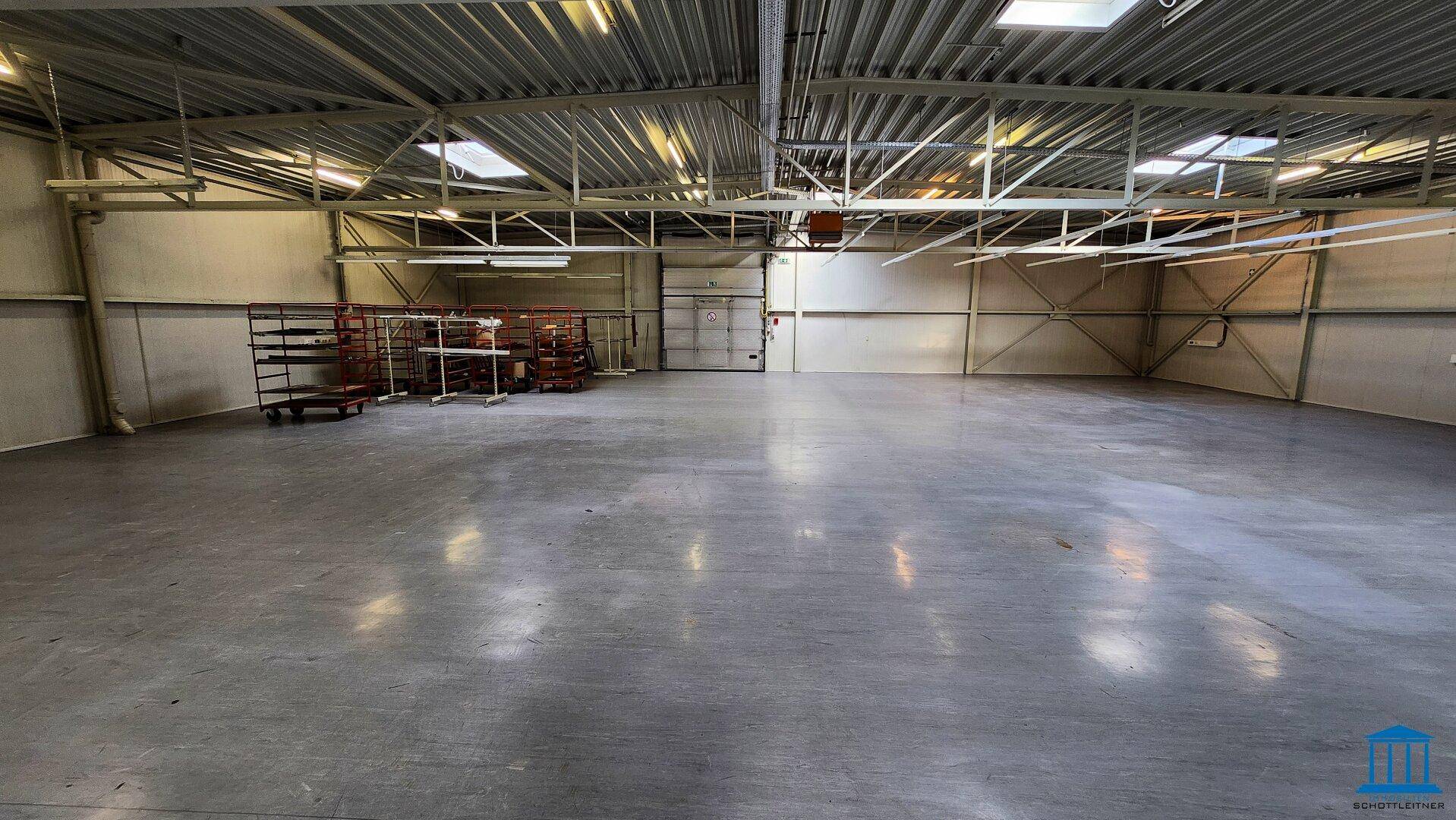 Weitläufige Lagerhalle mit Betonboden, Metallkonstruktion und Rolltor im Hintergrund, sehr geräumig.